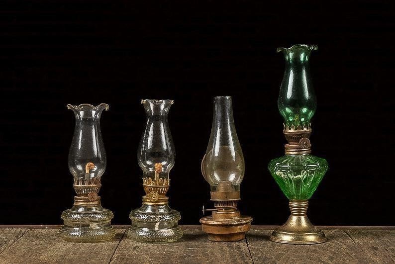 Set of (4) Miniature Oil Lamps: NOTE: For an accurate in-house shipping quote on this lot, please reach out to us at rockauctiongallery@gmail.com. Item SKU: C-13578 This lot includes (3) clear glass oil lamps and (1) lamp in emerald