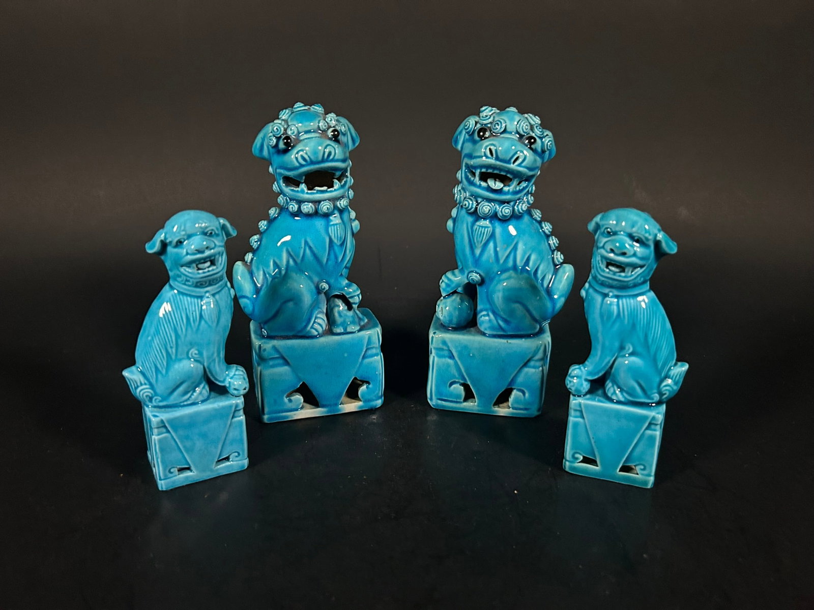 Two Pairs of Chinese Turquoise-Glazed Models of Buddhist Lions, Late Qing Dynasty/Republic Period: Consisting of both a larger and smaller set of Buddhist lions, each depicted in a seated position atop square pedestals, engaged in play with a brocade ball. They are intricately adorned with thick ey