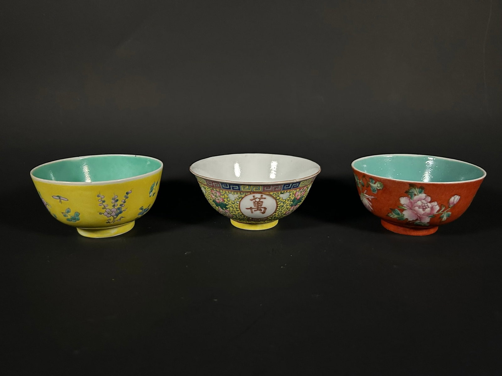 A Group of Three Chinese Famille Rose Bowls: Comprising a famille rose yellow-ground 'wan shou wu jiang' bowl, 2.3/8 in. (6 cm.) high, 5 in. (12.7 cm.) wide; a famille rose coral-ground 'flowers' bowl, 2.3/8 in. (6 cm.) high, 4.1/2 in. (11.4 cm.