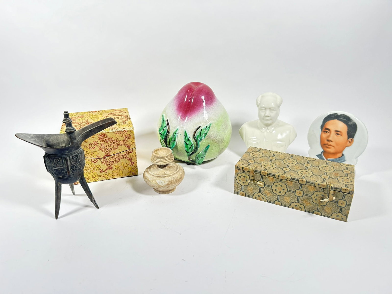 A Group of Seven Chinese Table Articles: Comprising two cloth boxes, the larger one measures 4.3/8 in. high, 5.1/2 in. wide, 5.1/2 in. deep; a famille rose temple altar peach, 7.1/8 in. (18.1 cm.) high, 7.1/4 in. (18.4 cm.) wide; a pottery m