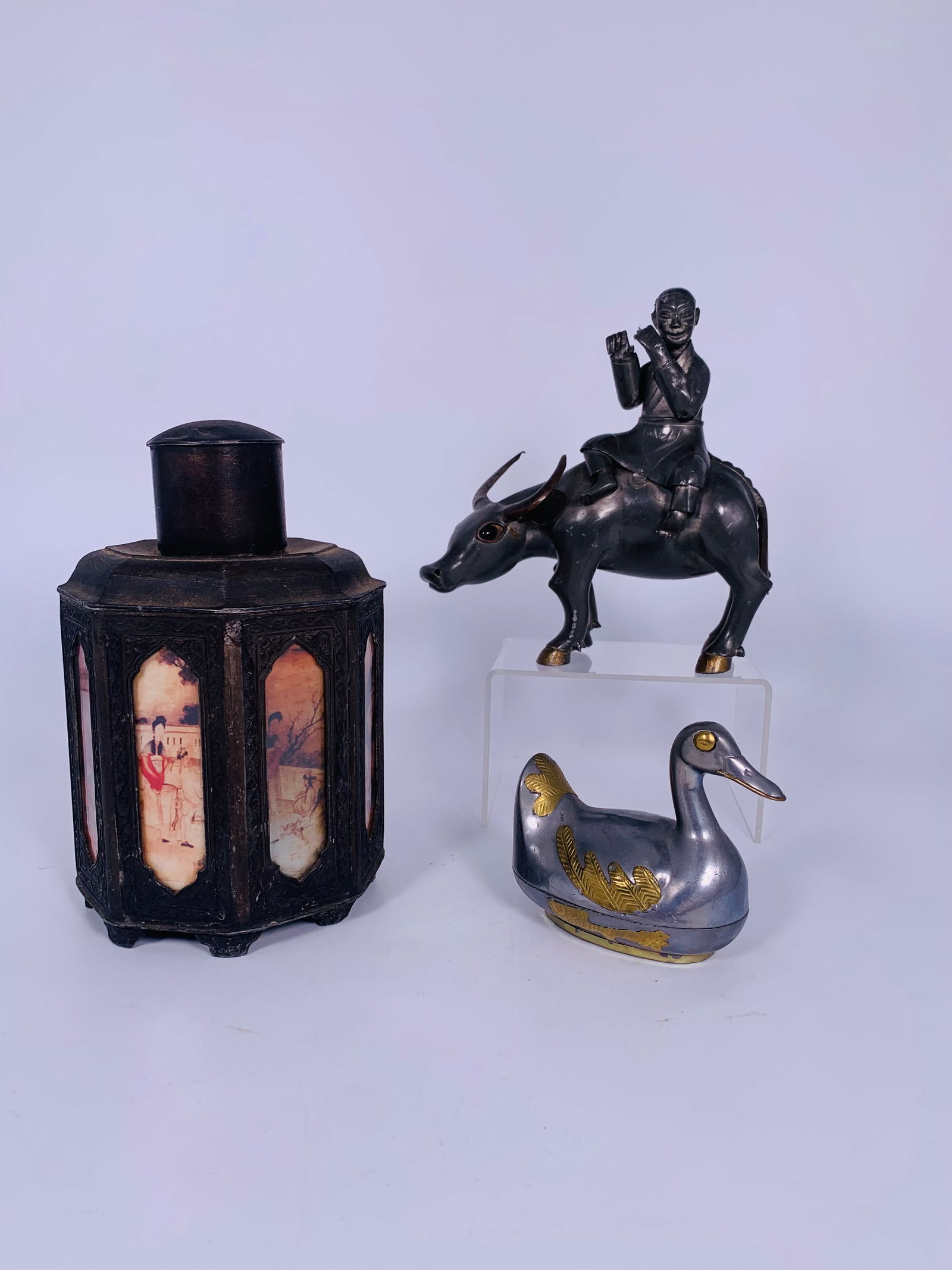 A Group of Three Chinese Metal Table Objects: Comprising a polished bronze buffalo and rider sculpture, 6.5/8 in. high, 6.1/4 in. wide; a pewter duck trinket box and cover, 3.1/4 in. high, 4 in. wide; and a vintage tin tea caddy, with manufacture
