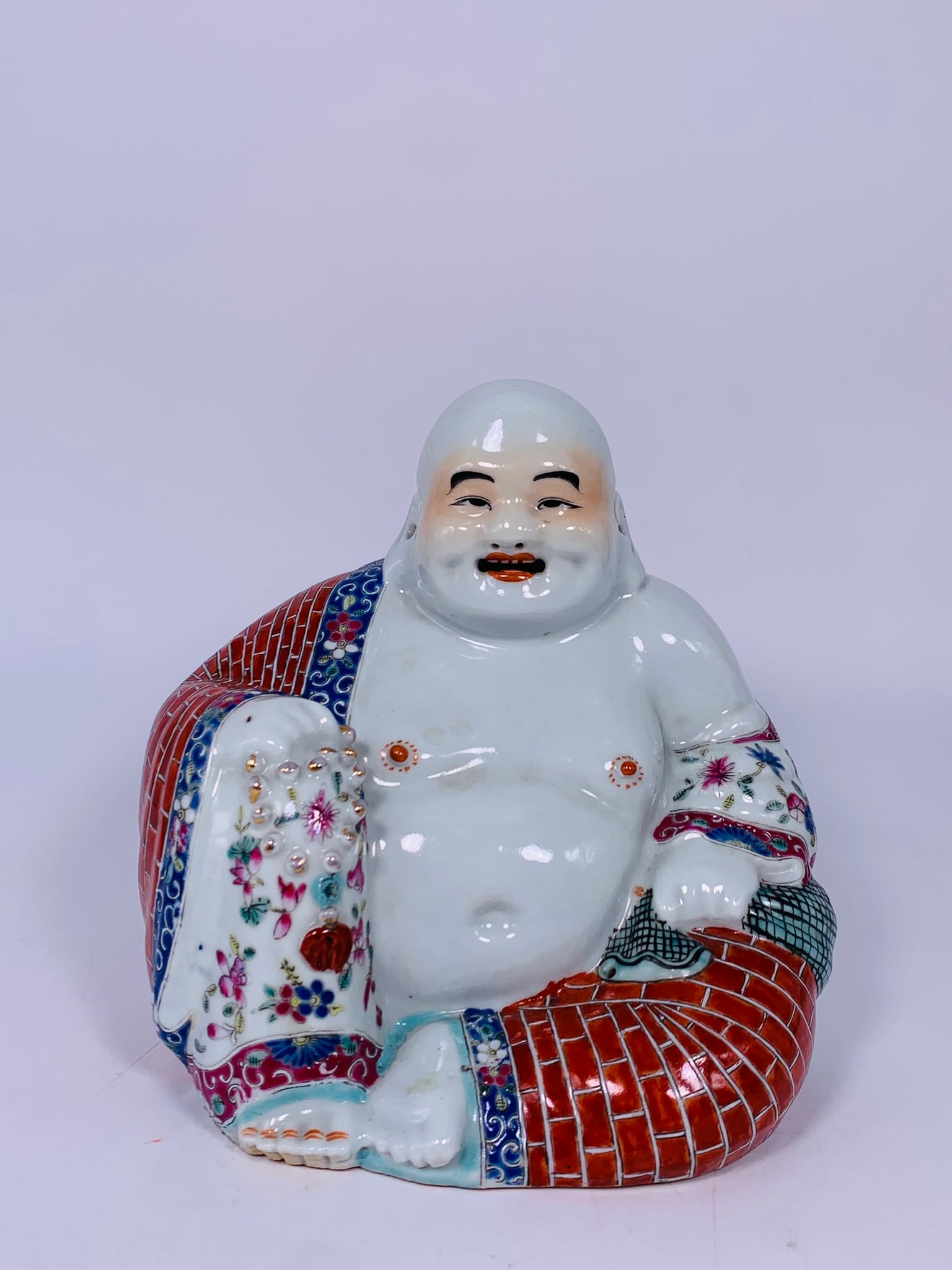 A Chinese Famille Rose Figure of Budai, Zhu Mao Ji Zao Mark: The figure is modeled seated, holding a string of prayer beads in his right hand. The base is stamped with the seal mark 'Zhu Mao Ji Zao'. 8 in. high, 7.1/2 in. wide.