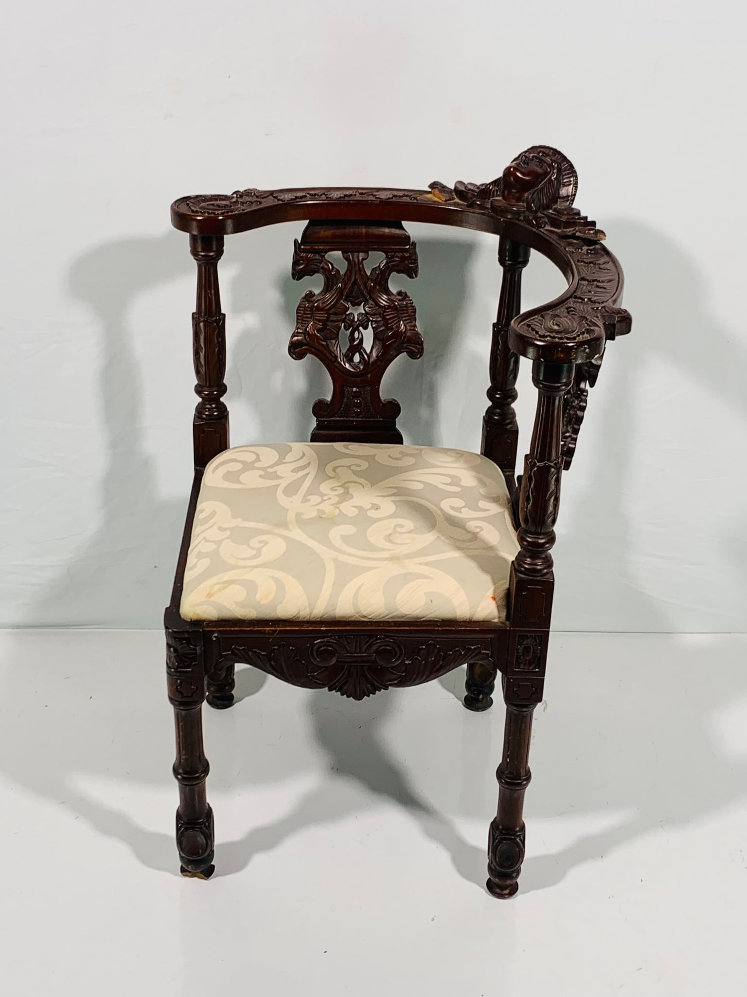 An Italian Antique Victorian Carved Mahogany Corner Armchair, Late 19th Century: The chair features a curved toprail with a putti head at the center, and a drop-in seat supported by four legs. 35 in. high, 27 in. wide, 26 in. deep. Close comparable please see A Pair of North Itali