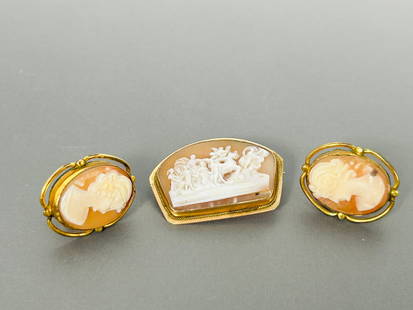 A Group of Three Vintage Cameo and Gold Pins: Comprising an ornate angelic scene carved cameo and gold pin, 1.1/4 in. long, 3/4 in. wide; and a pair of carved cameo and gold pins, 7/8 in. long, 3/4 in. wide each.