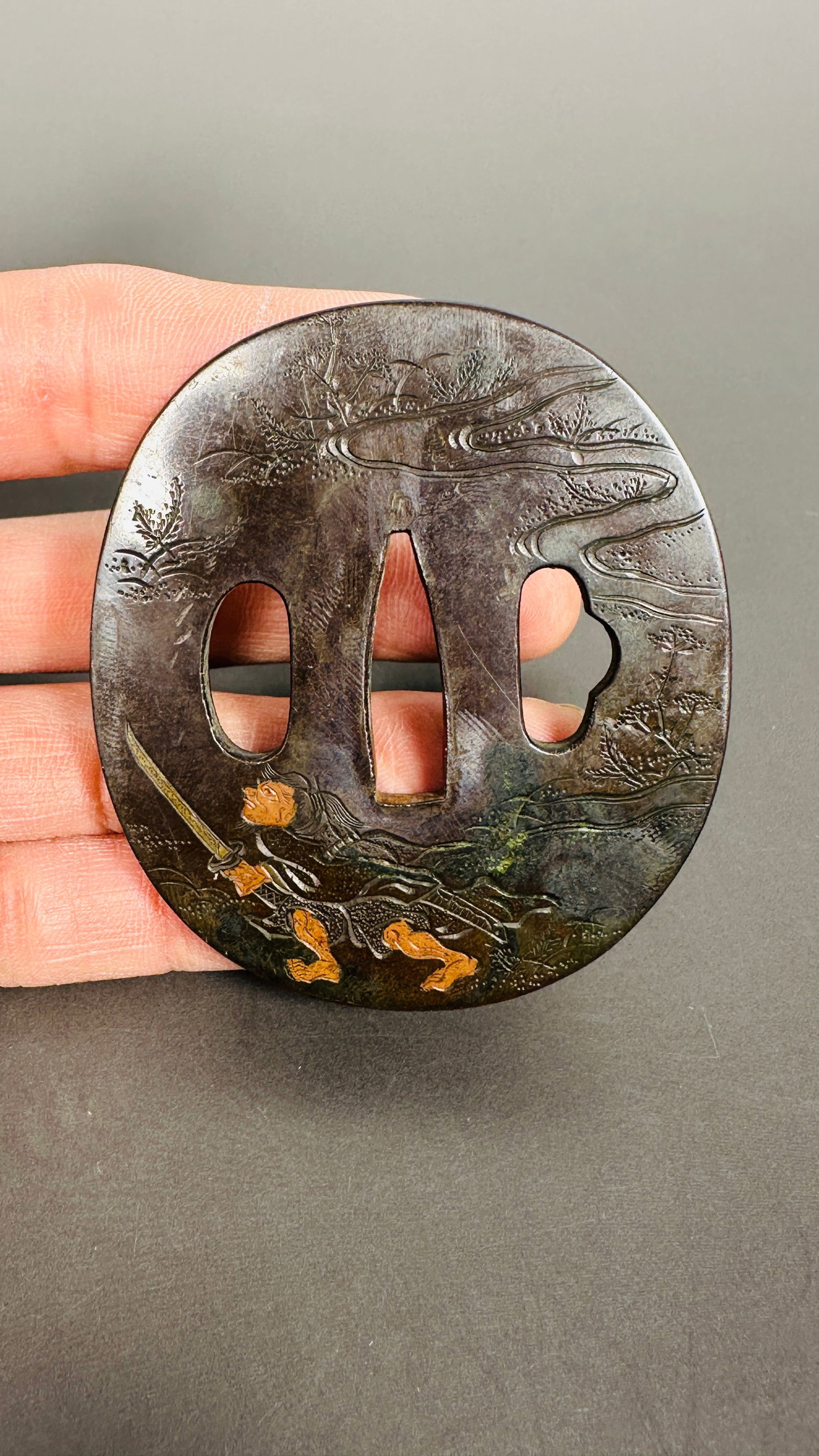 A Japanese Iron Sword Tsuba: A finely crafted Japanese iron tsuba (sword guard) designed a figure with sword in a landscape. 2.5/8 in. long, 2.1/4 in. wide.