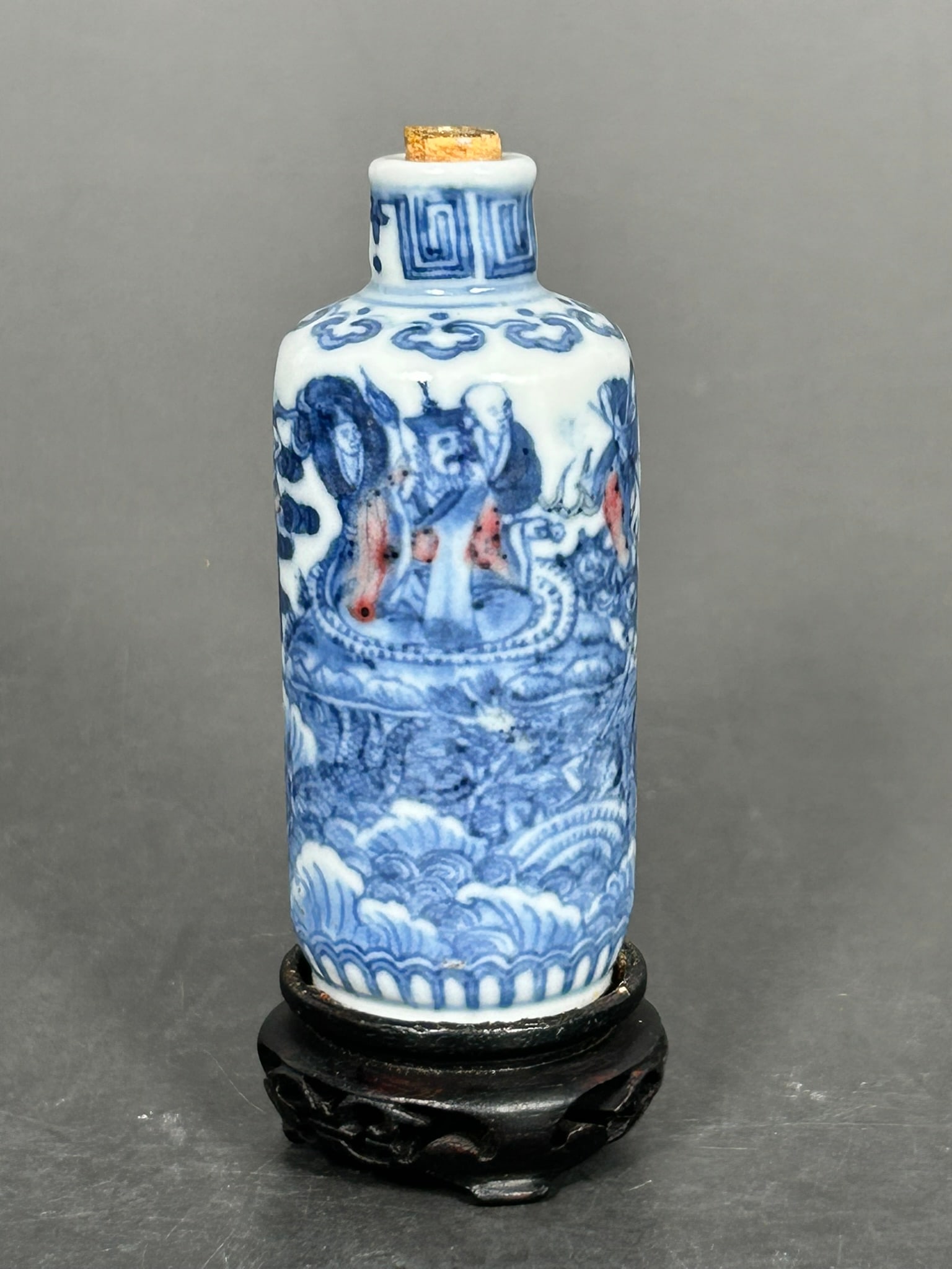 A Chinese Underglaze-Blue and Copper Red Decorated 'Immortals' Snuff Bottle: With a wood stand, 2.7/8 in. high, 1.1/4 in. wide for the snuff bottle.