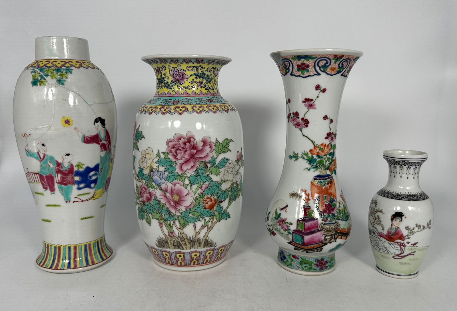 A Group of Four Chinese Famille Rose Vases, 20th Century: Comprising an inscribed 'peony' vase, 9.5/8 in. high, 4.3/4 in. wide; a 'lady and boys' vase, 10.3/8 in. high, 4.1/4 in. wide; a 'antiques' vase, 9.3/4 in. high, 4 in. wide; and a small inscribed 'lad