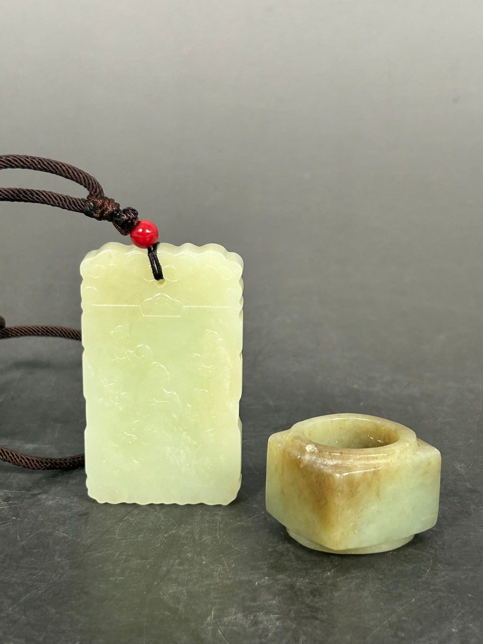 Two Chinese Jade Objects: Comprising a carved greenish-white jade 'five boys' plaque, 2.3/8 in. high, 1.3/8 in. wide; and a celadon and russet jade cong, 7/8 in. high, 1.1/8 in. wide.