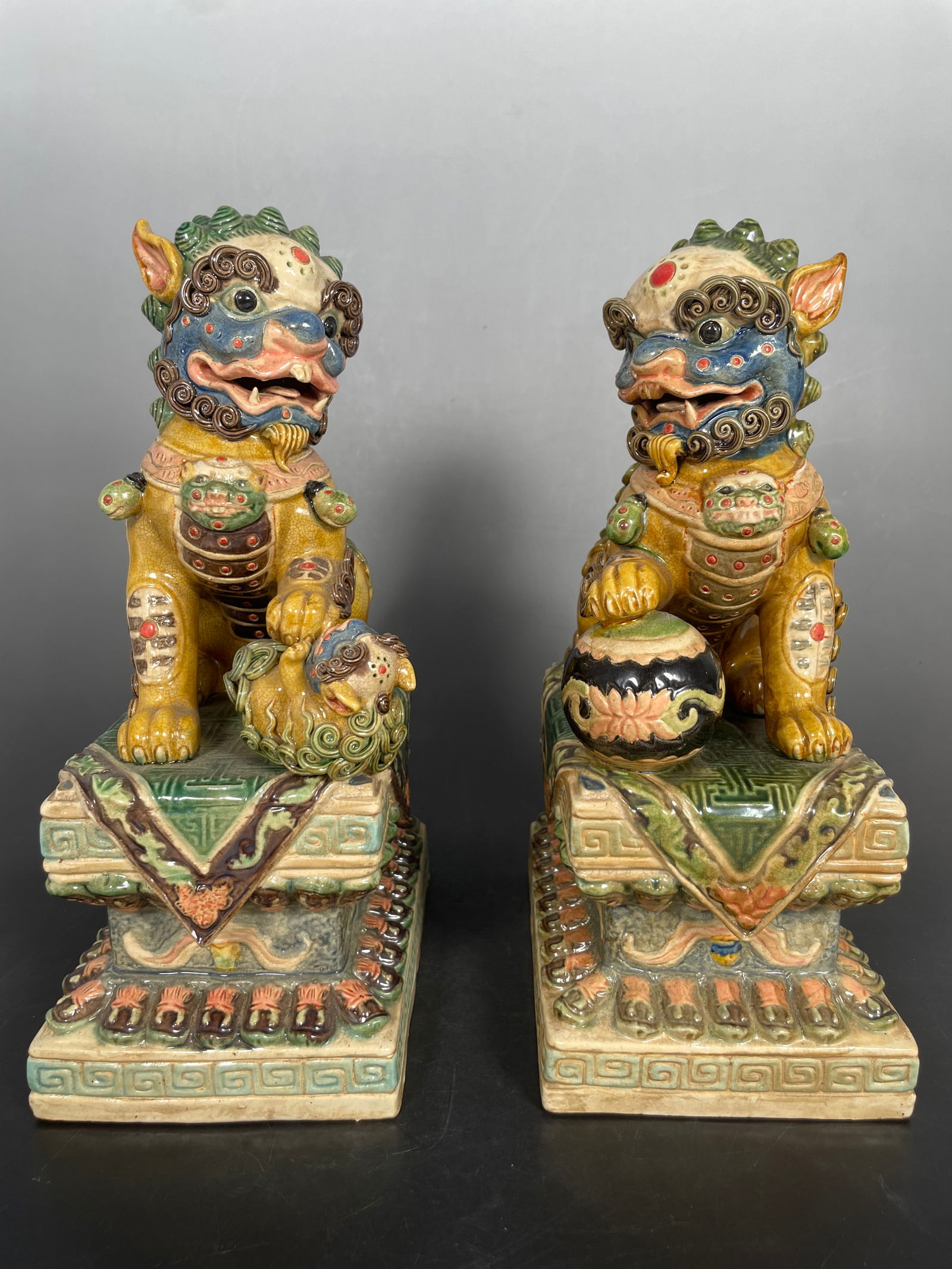A Pair of Chinese Painted Pottery Figures of Buddhist Lions: Maker's mark to the undersides of both. 11 in. high, 7.1/4 in. wide each.