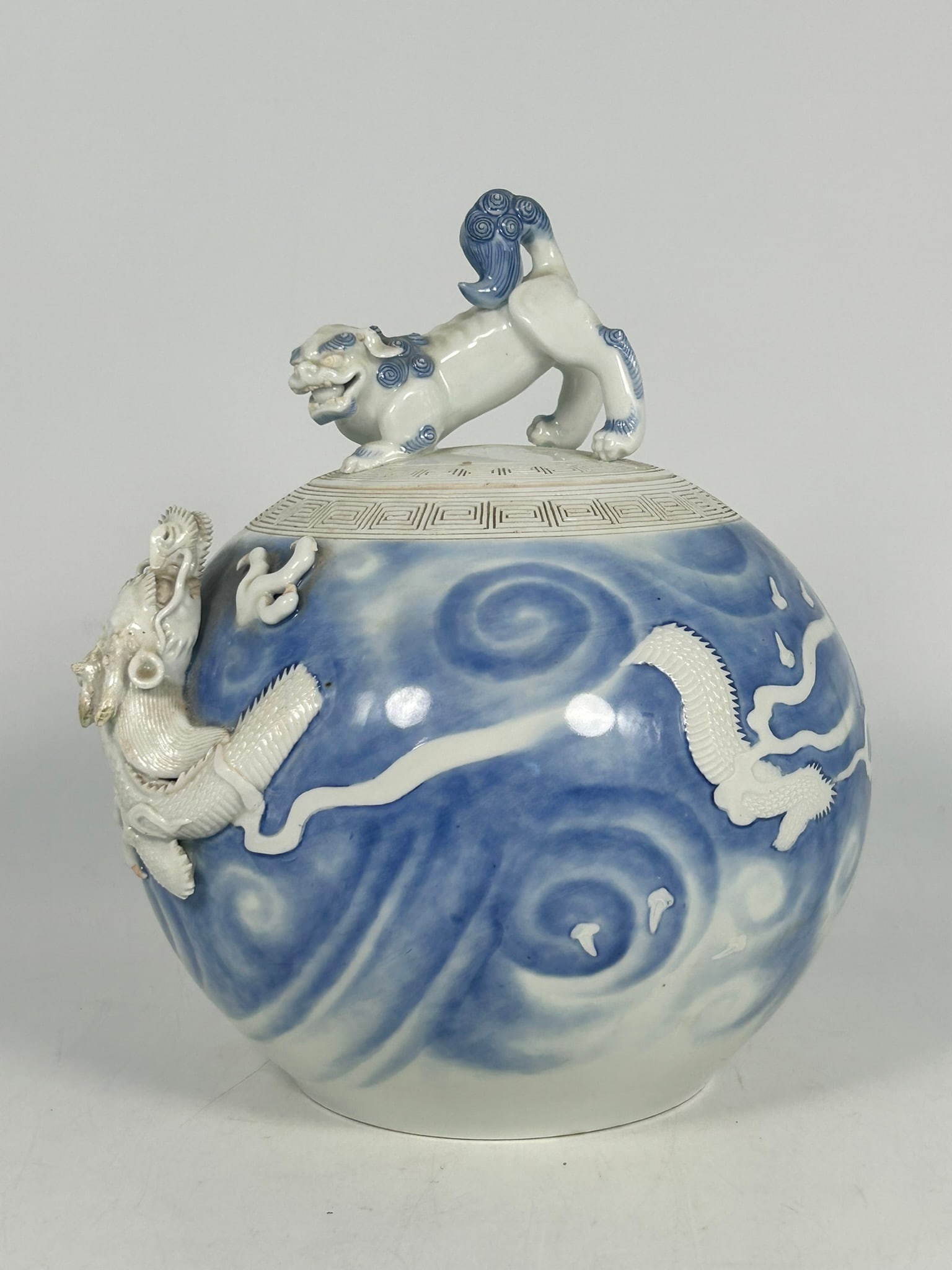 A Japanese Hirado-Style Blue and White Jar and Cover: Globular in form, decorated in underglaze blue with a dragon, high-relief for the head and low-relief for the body, in flight amid swirling clouds, the rim encircled by an incised key-fret border. The