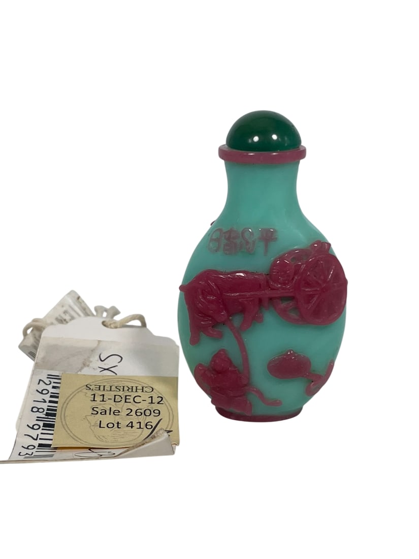 Christie's Provenance: A Chinese Pink Overlay Pale Turquoise Glass Snuff Bottle: Carved with a scene of a boy leading a buffalo pulling a cart, the reverse depicting an equestrian hunter accompanied by a dog, and fitted with a glass stopper. 2.5/8 in. high, 1.3/8 in. wide overall.