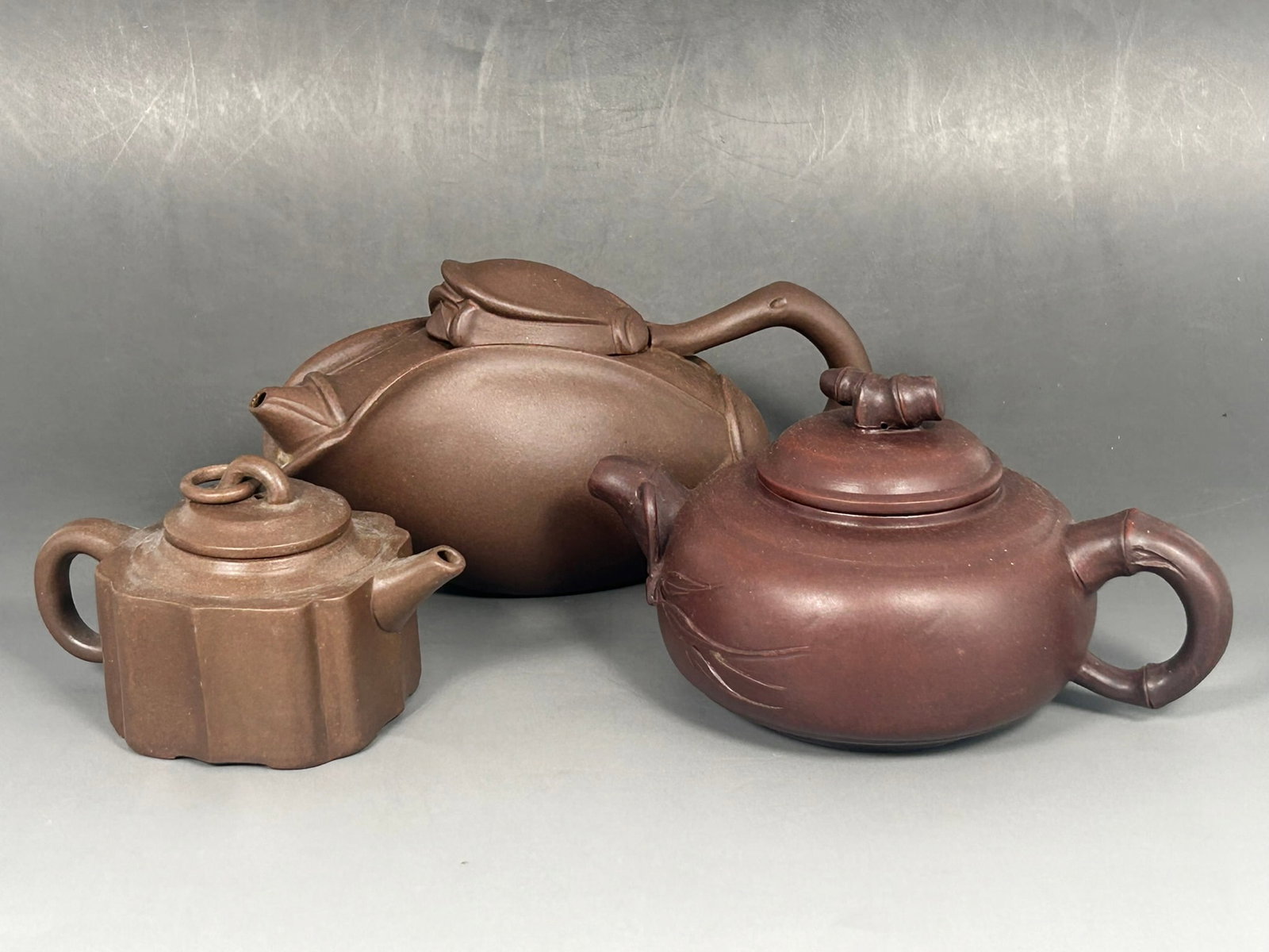 A Group of Three Chinese Yixing Pottery Tea Pots and Covers: The longer one has maker's marks to the underside of the teapot, inner side of the cover, and bottom of the handle, 3.1/4 in. high, 7 in. wide; the mid-sized one has maker's marks to the underside of