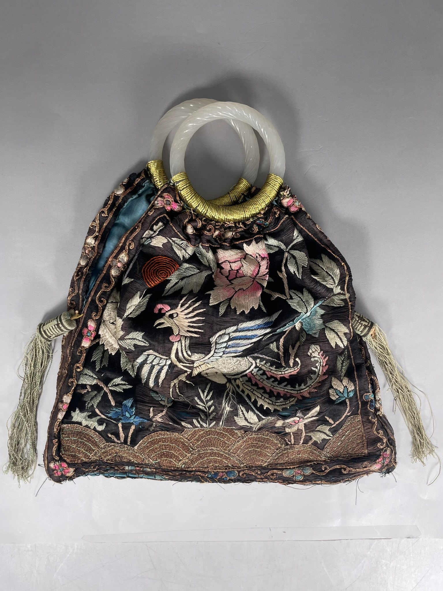 A Chinese Embroidered Silk Handbag: With two carved white jade bangles as handles. The bag measures 11 in. long, 10.1/4 in. wide.