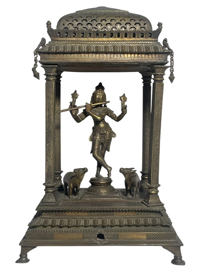 An Antique Indian Bronze Shrine with a Figure of Krishna: The figure is housed within a decorative architectural structure, commonly referred to as a mandir or temple shrine. It depicts Krishna as a youthful deity, often associated with joy and playfulness. 