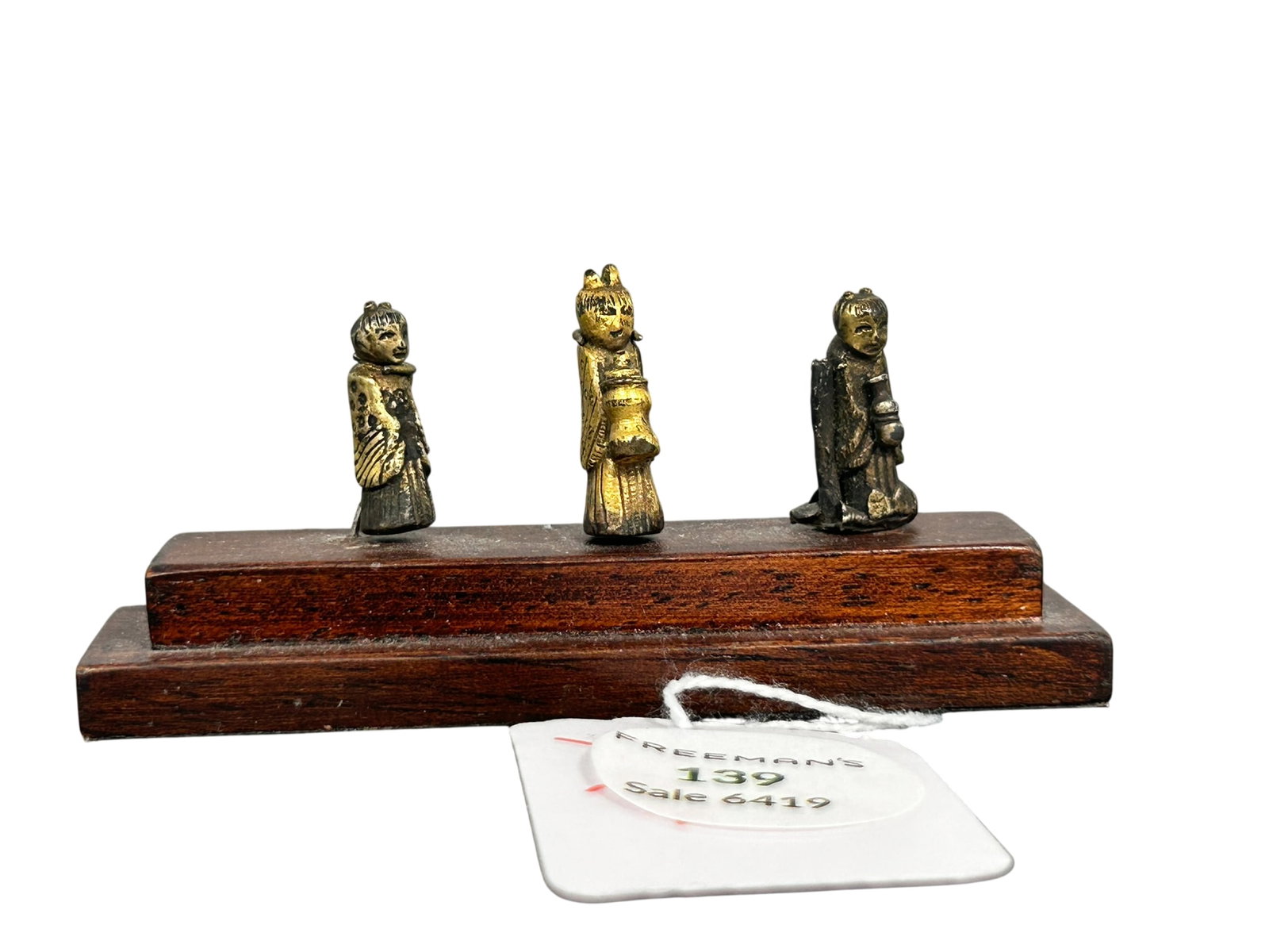 Freeman's Provenance: An Unusual Group of Three Chinese Gilt Bronze Miniature Deities, Ming Dynasty: Two holding vessels, one with an associated slender tube to one side; mounted on a later wood stepped base. The tallest miniature figure measures 1 in. high; 1.5/8 in. high, 3.1/2 in. wide overall inc