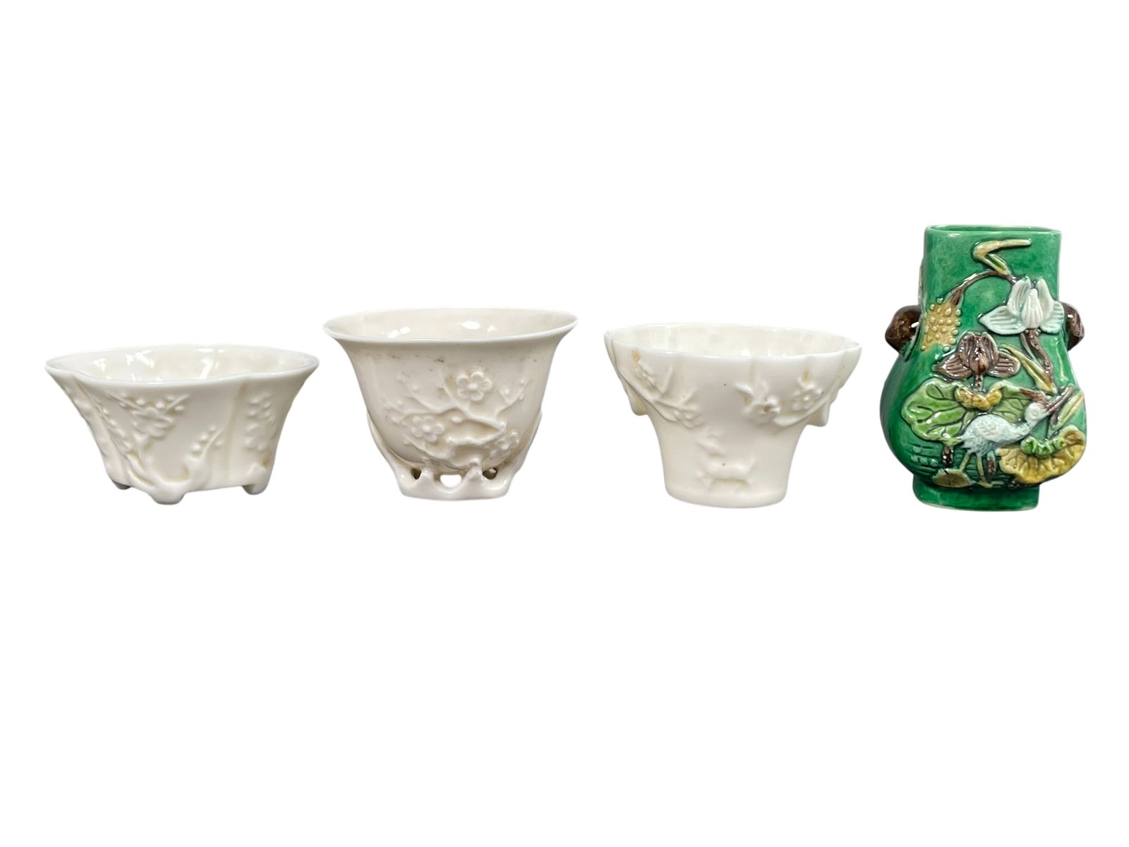A Group of Four Chinese Small Porcelain Vessels: Comprising a group of three dehua libation cups, with the tallest measures 1.7/8 in. high, 2.5/8 in. wide; and a molded 'cranes and lotus pond' vase, 3 in. high, 2 in. wide.