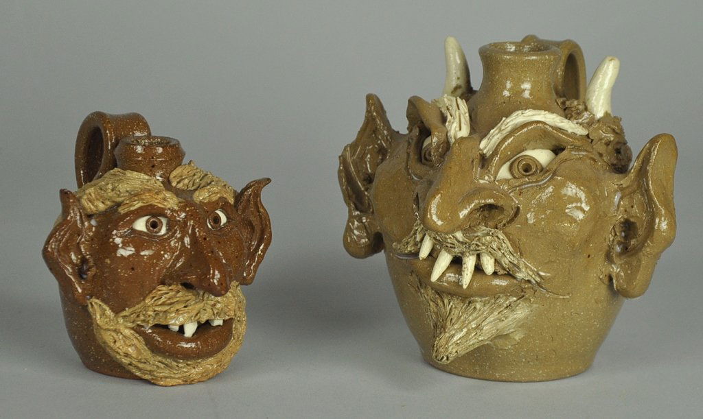 Two North Carolina North Cole Pottery Face Jugs: One devil style face jug with pointed ears and pointed teeth, 4" H. Signed on base, "North Cole Pottery/1992/Sandy Cole." One of grinning man with beard and pointed ears, 3" H. Signed on base, "North