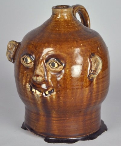 North Carolina Meaders Face Jug: In brown glaze with noticeably pooled glaze at base. Signed on base, "Meaders" (above line illegible due to glaze run, but possibly Reggie). 8 1/2" H. From the collection of Howard and Anne Smith of M