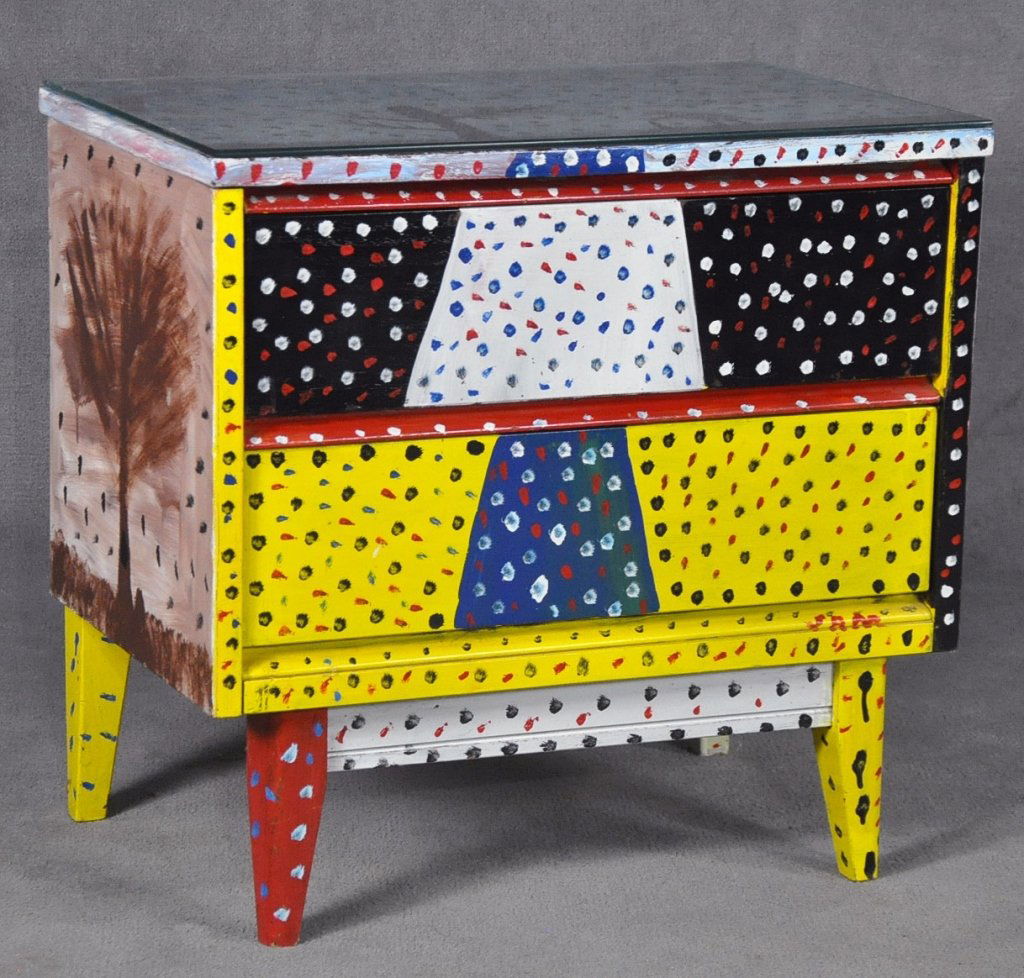 Sam McMillan Two-Drawer Cabinet: American - N.C., born 1926. Also known as "Sam the Dot Man." Top painted with dog in boots with umbrella, squirrel in bare tree, and multi colored leaves. Front with polychrome spotted design. Trees o