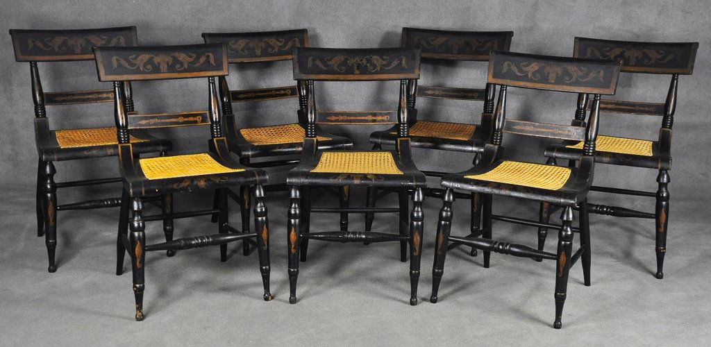 Set of Seven "Fancy Baltimore" Chairs: Circa 1840. All with gilt Classical motif stencil decoration on black ground. Having handwoven caned seats - three recently recaned. 17" seat height. One with reduced height. Though it can not be veri