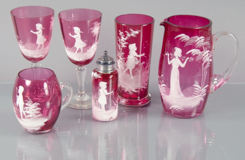 Six Mary Gregory Cranberry Glass Items: Including one pitcher, 5 3/4" H.; one vase, 6 3/8" H.; one handled cider cup, 3 1/2" H.; two wines, 5 3/4" H.; and one shaker, 4" H. Each decorated with white enamel figures of children or young woman