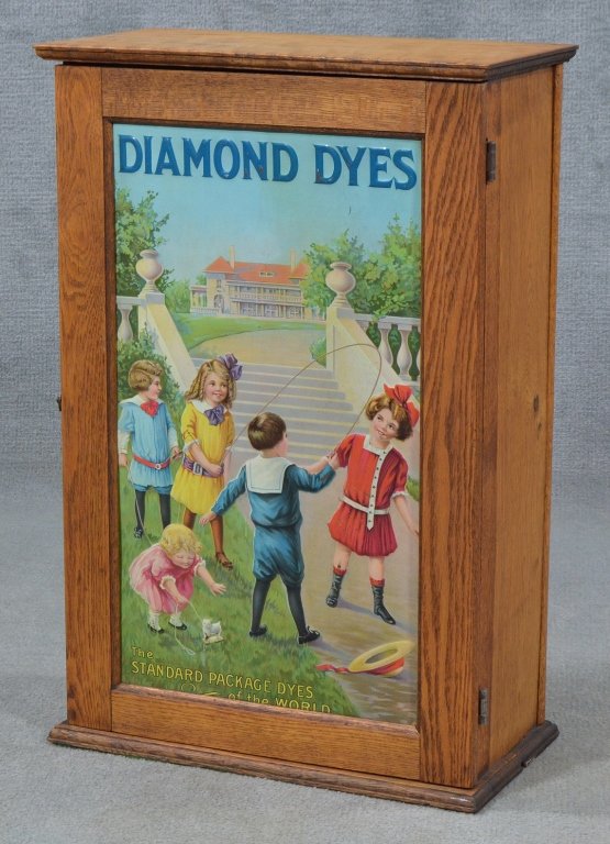 Diamond Dyes Cabinet: Having colorful original tin lithograph showing children playing. Interior with 36 divided compartments for dye packets. Oak case with hinged door. Apparently original finish. 24 1/2" x 16" x 8 1/2".