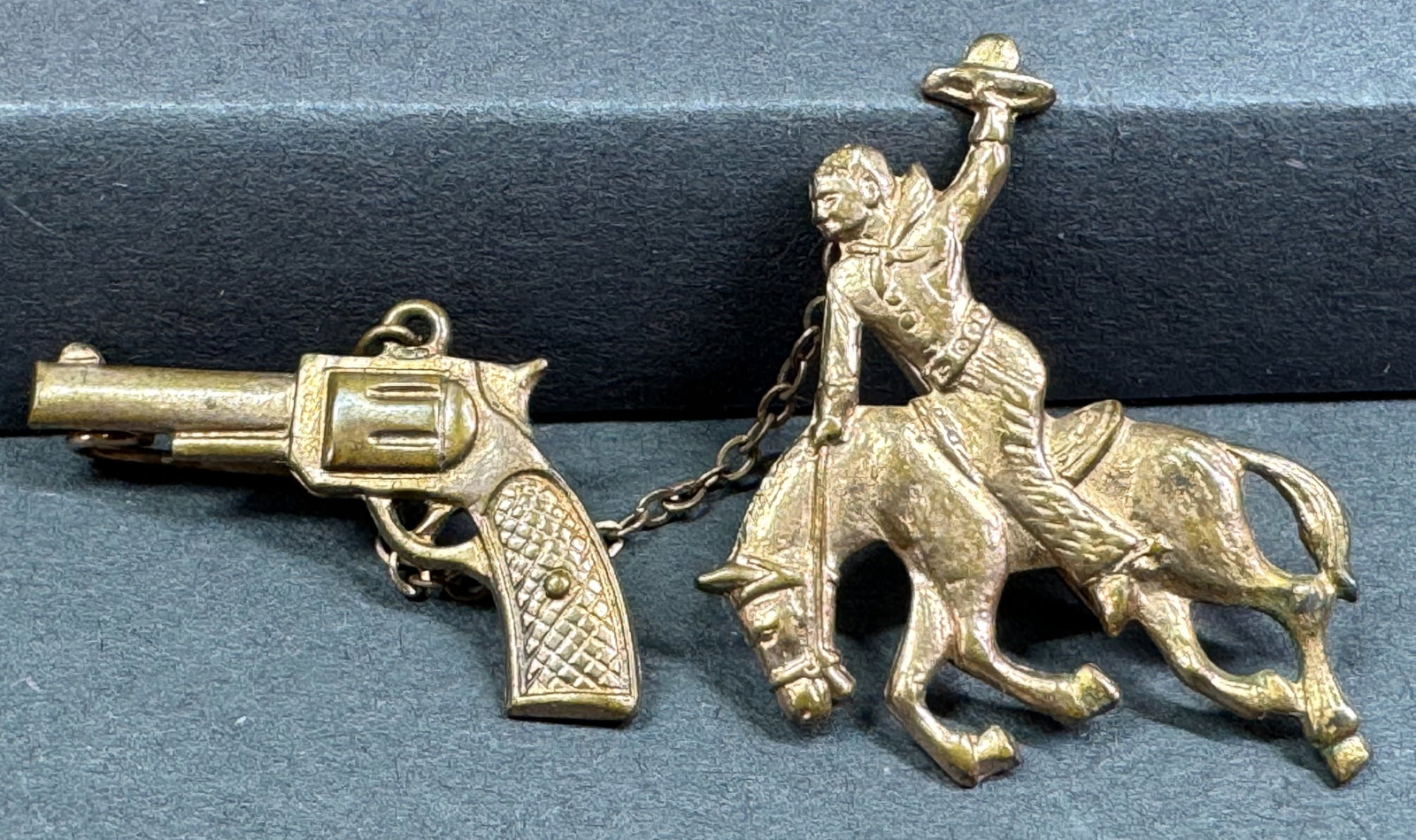 Vintage cowboy days revolver chained to a horse rider goldtone metal pin brooch.: Vintage cowboy days revolver chained to a horse rider goldtone metal pin brooch. Unmarked. For measures please refer to the pictures taken with a measuring tape. Weight: 5 Grams. This is a NO RESERVE 