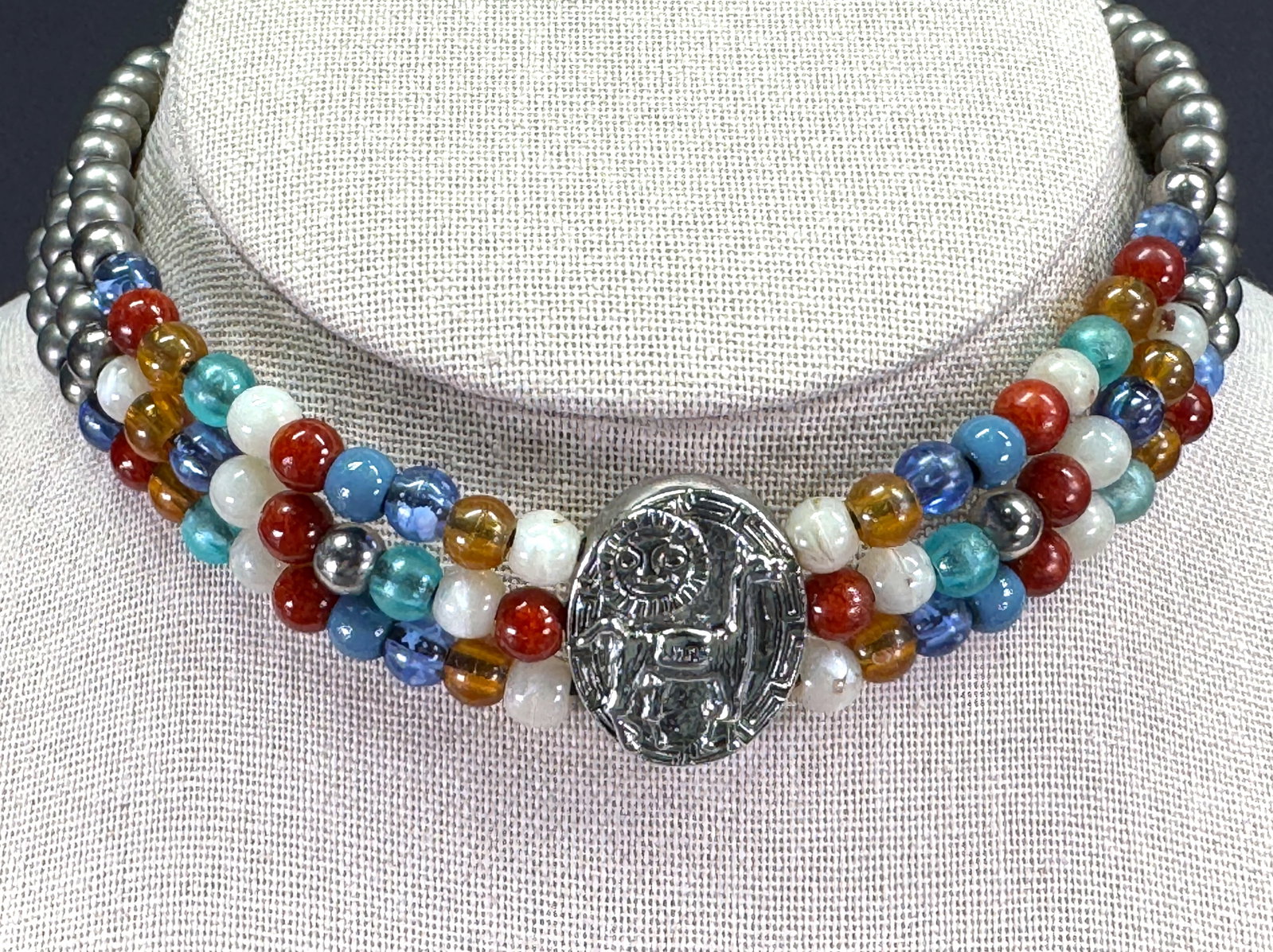 Vintage ethnic silvertone metal lama medallion & charm color plastic beaded choker neckalce: Vintage ethnic silvertone metal lama medallion & charm color plastic beaded choker neckalce. Unmarked. For measures please refer to the pictures taken with a measuring tape. Weight: 32 Grams. This is 