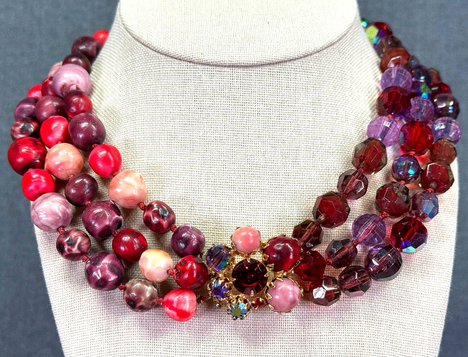 Vintage Haskell style crystals and coated glass beads flower clasp collar necklace: Vintage Haskell style berry colors crystals and coated glass beads 3 strands collar necklace. Sliding side goldtone ,eyal flower clasp. Unmarked. For measures please refer to the pictures taken with a