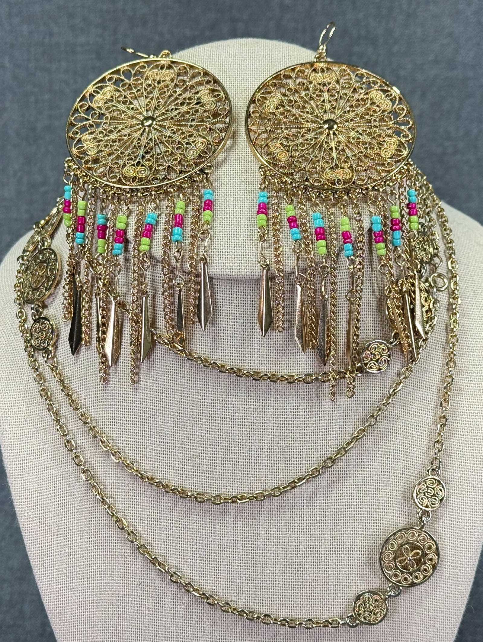 Tribal style goldtoned metal filigree medallions necklace & glass beaded fringe hook earrings: Tribal style goldtoned metal filigree medallions necklace & glass beaded fringe hook earrings. Unmarked. For measures please refer to the pictures taken with a measuring tape. Weight: 54 Grams. IN HOU