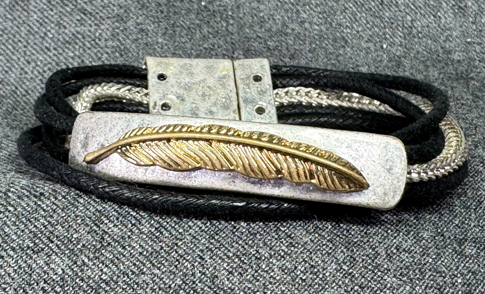 Feather charm magnetic bracelet #a: Feather charm magnetic bracelet. Textured silver-toned. gold-toned metal, rope and chain strings. Unmarked. For measures please refer to the pictures taken with a measuring tape. Weight: 25 Grams. IN