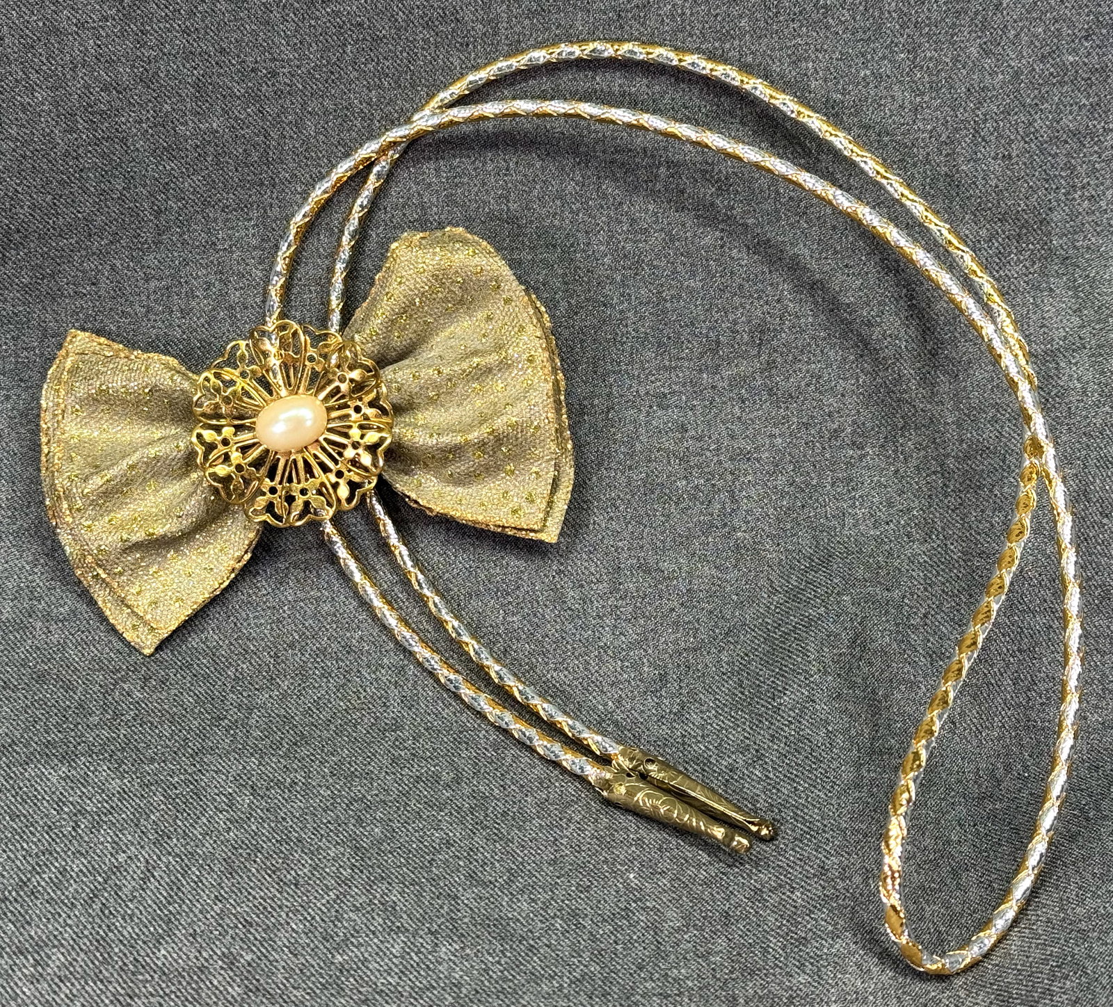 Vintage Bolo Slide Necklace with Jeweled Glitter Fabric Bow. Gold/Silver woven cord. *M: Vintage Bolo Tie Necklace with Jeweled Glitter Fabric Bow. Pearly cab gold-tone filigree flower. Gold/Silver woven cord. Unmarked. For measures please refer to the pictures taken with a measuring tape