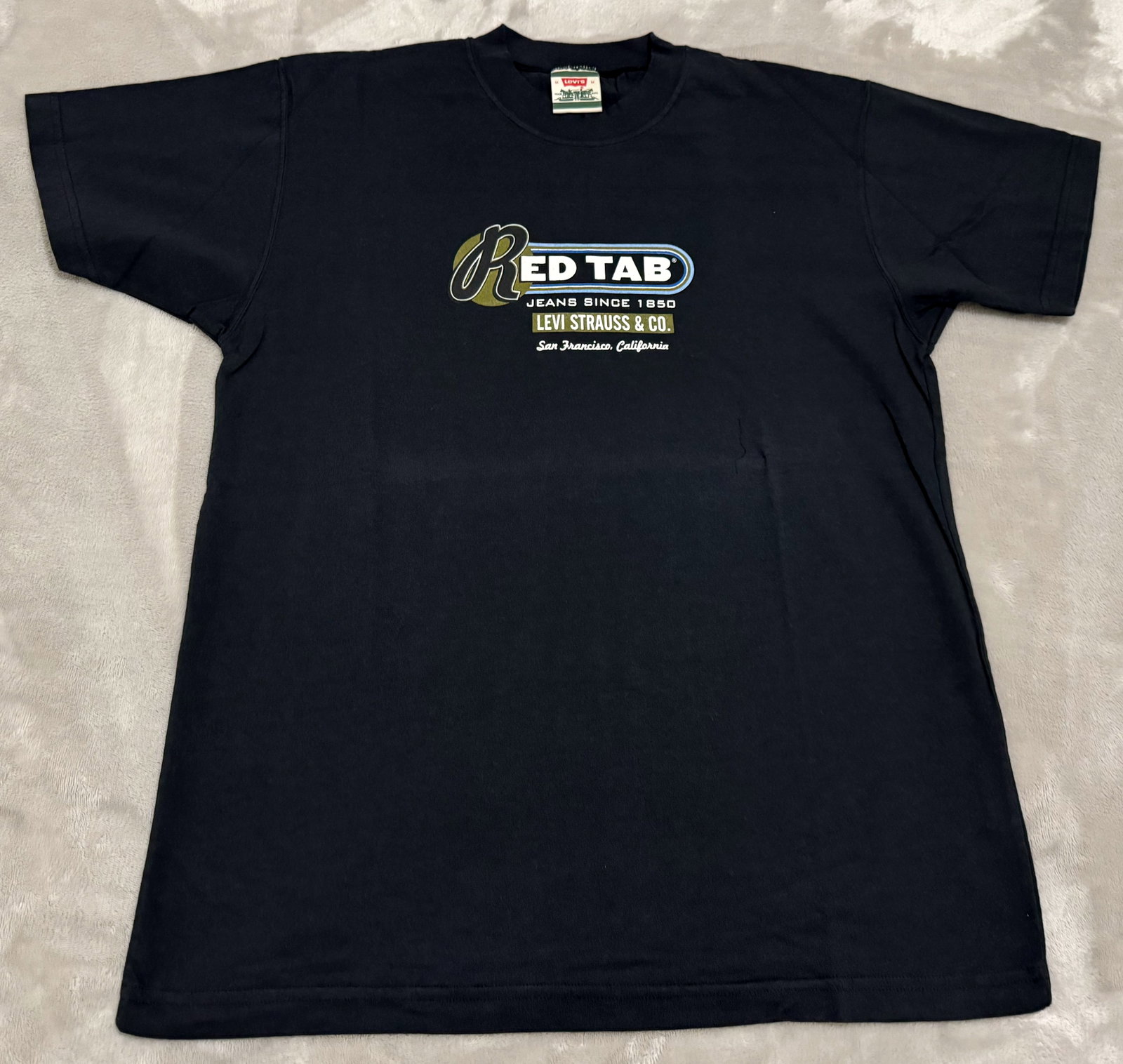 NOS 90s Vintage Levis Black Red Tab Jeans San Francisco Tee Shirt: Unused Features a colorful vintage chest graphic highlighting the classic "Red Tab" line with supporting "Jeans Since 1850 / Levi Strauss & Co. / San Francisco, California" multi-font typography True 