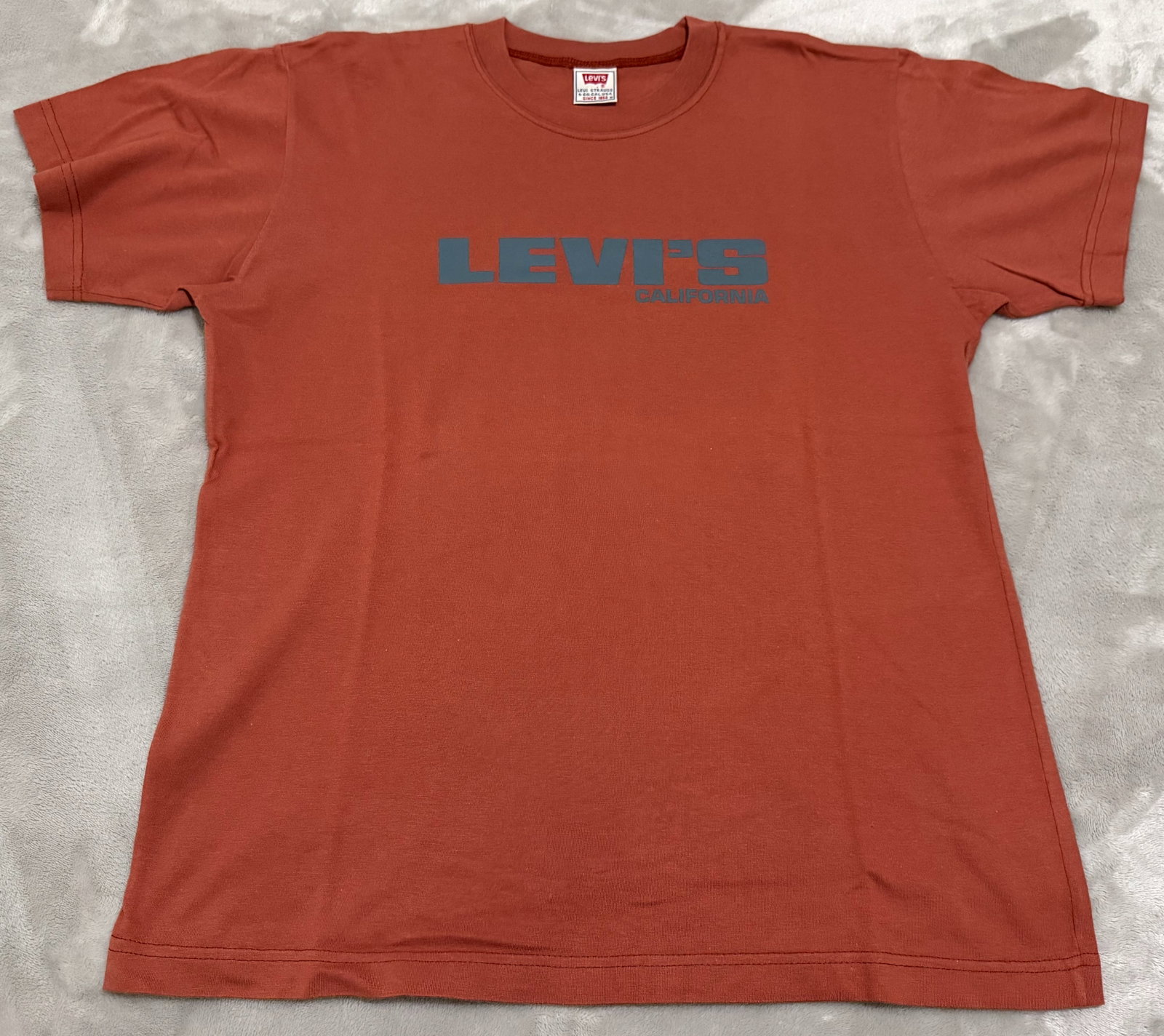 NOS 90s Vintage Levis Terracotta Rust Orange Block Logo Tee Shirt: Unused Features a minimalist, retro block-lettering "LEVI'S / CALIFORNIA" chest graphic screenprinted in a tonal slate blue. True vintage 1990s Levi Strauss & Co. short-sleeve crewneck t-shirt. 100% C