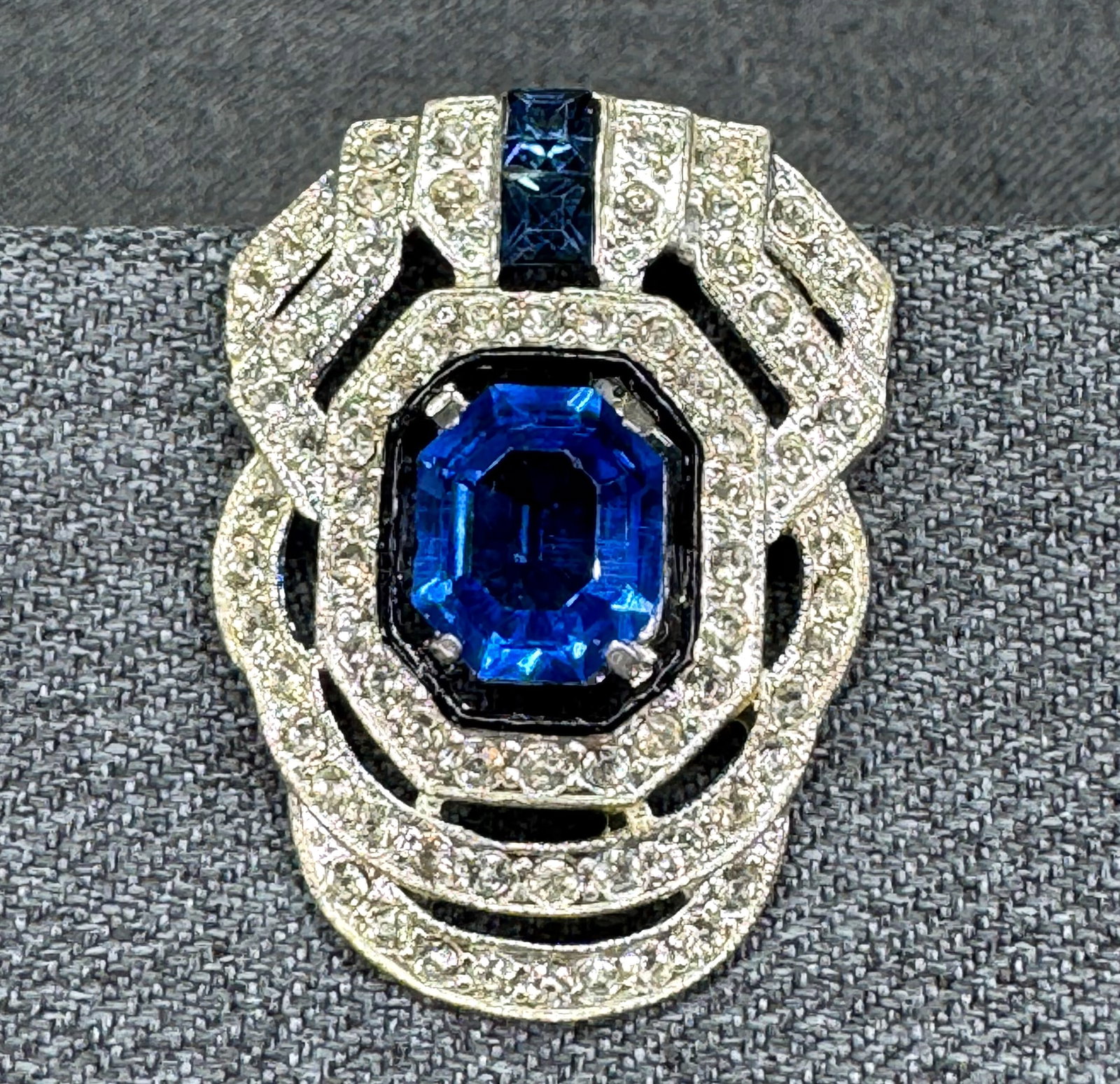 1930s Art Deco Pave Rhinestone Sapphire-Blue Pot Metal Dress Clip. *p: Antique Art Deco dress clip featuring a large faux sapphire crystal top square-cut and centered in a black enamel tiered pot metal frame, accented with pave-set clear rhinestones. Unmarked. For measur
