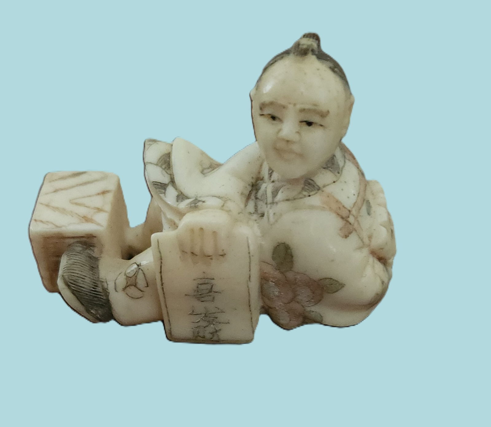 SIGNED ANTIQUE JAPANESE BONE NETSUKE THE NUMBERS MAN: Antique Japanese carved bone netsuke of a seated man with a box and the old numbers game. Artist signed. With Himotoshi (two holes) used for the cord to attach the Netsuke to the obi. Measures 2 1/8".