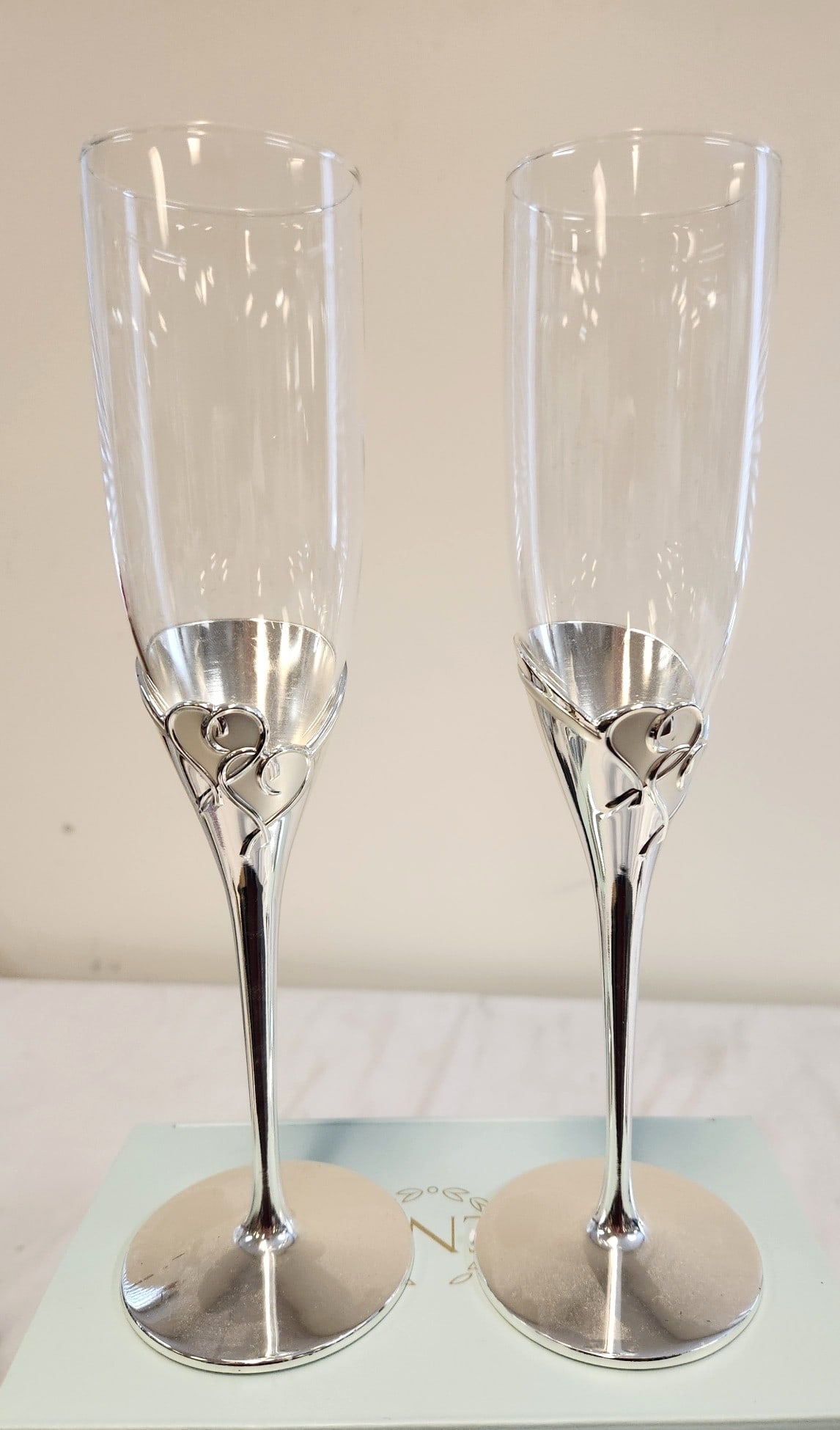 LENOX TRUE LOVE TWO PIECE TOASTING SET: Lenox True Love Two Piece Toasting Set. Pristine still in box. Both flutes are silver-plated and feature the design of two interlaced hearts. Each measure 9.5" tall and total lot weight is 1 lb 4 oz.