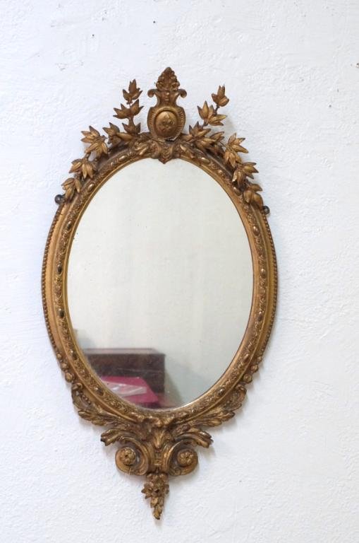 Antique English gilt oval wall mirror circa 1850: English, gilt, oval wall mirror with hand carved floral and leaf decoration and shield center design. 3" frame, bead trim, old silvering on mirror - - measures42" x 22"