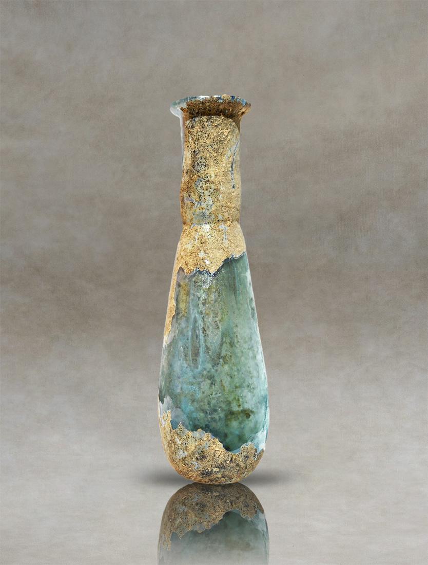 Ancient Roman Glass Unguentarium: An ancient Roman glass unguentarium. It has a pyriform body, with a cylindrical neck tapering at the base, and a bent and everted rim. Colorless glass with a layer of natural and lovely iridescence.In