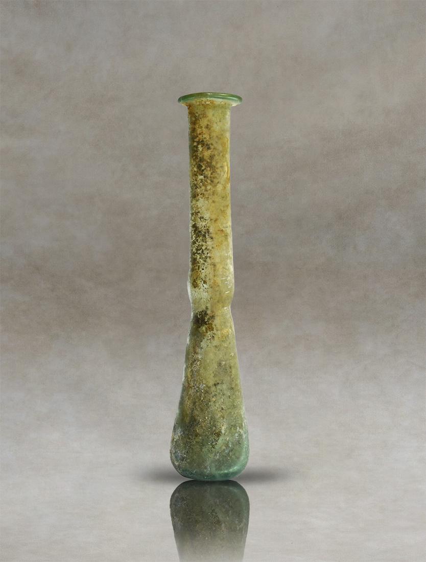 Roman Glass Unguentarium Perfume Bottle: Roman unguentary of green pale colourless blown glass, probably used as a perfume bottle. The vessel has a flattened rim and a long, narrow cylindrical neck that widens towards the body. The lower par