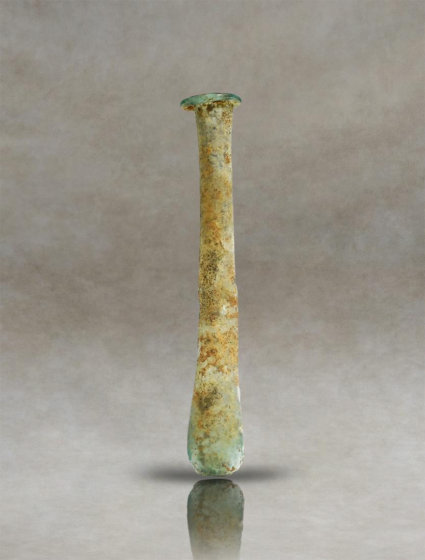 Roman Glass Unguentarium: Roman unguentary of blue pale colourless blown glass, used as a perfume bottle. The vessel has a flattened rim and a long, narrow cylindrical neck that widens towards the body. The lower part of the c