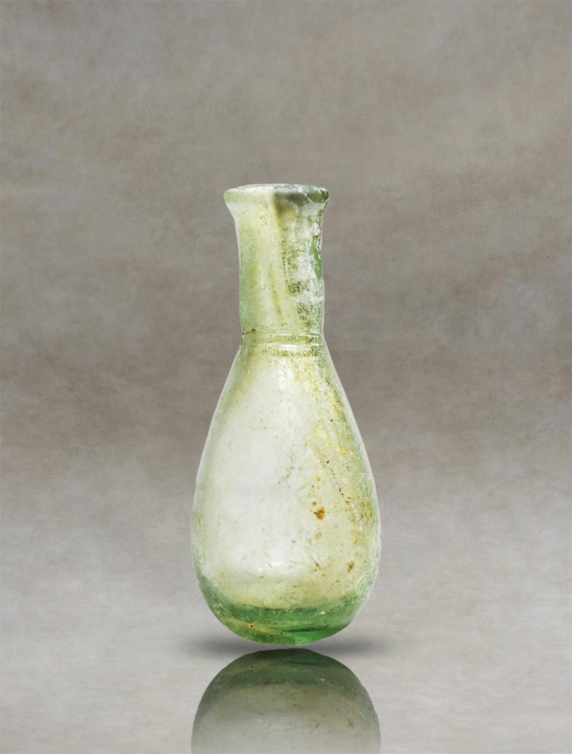 Roman Glass Unguentarium: Discover the beauty of Roman blown glass with this exquisite artifact. Made from pale glass, it features a small piriform body, cylindrical neck, and everted rim. The colorless glass is adorned with a