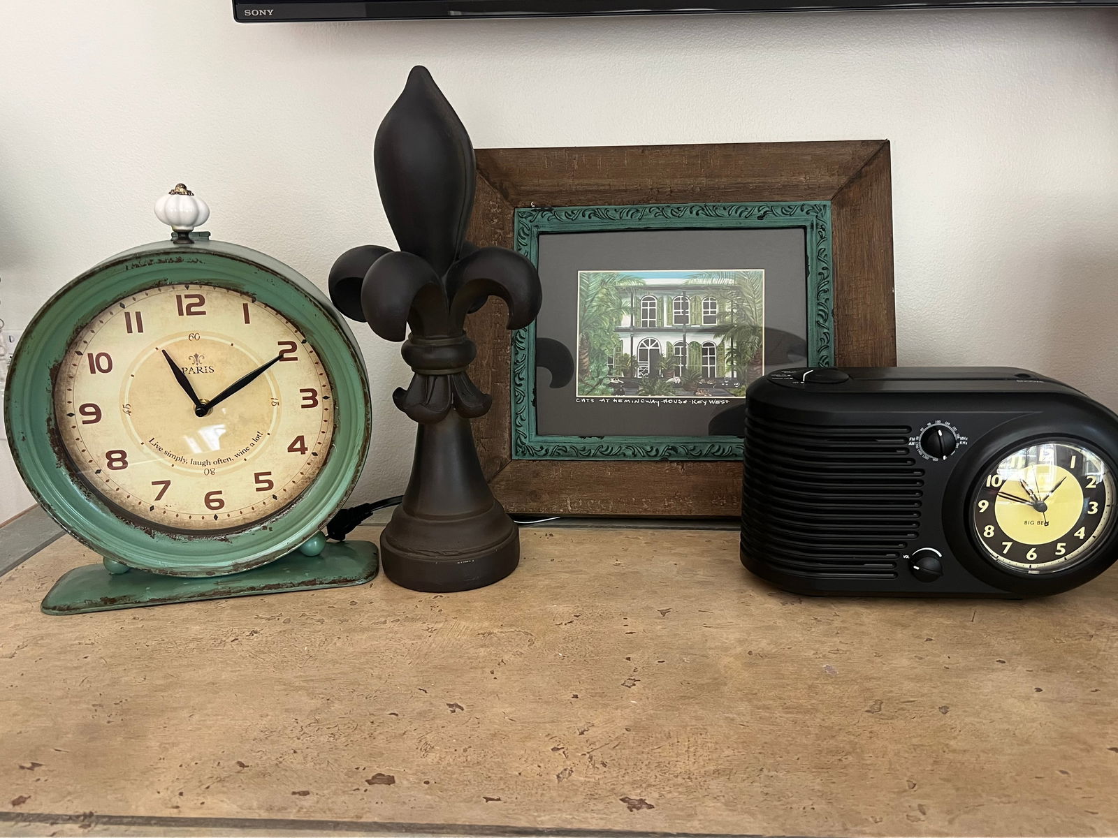 Decorative Grouping: Grouping of decorative objects including am old school clock-radio, a Paris style clock, a Fleur de Lis object and a Key West print titled "Cats at the Hemingway House, Key West" signed Black. Dimensi