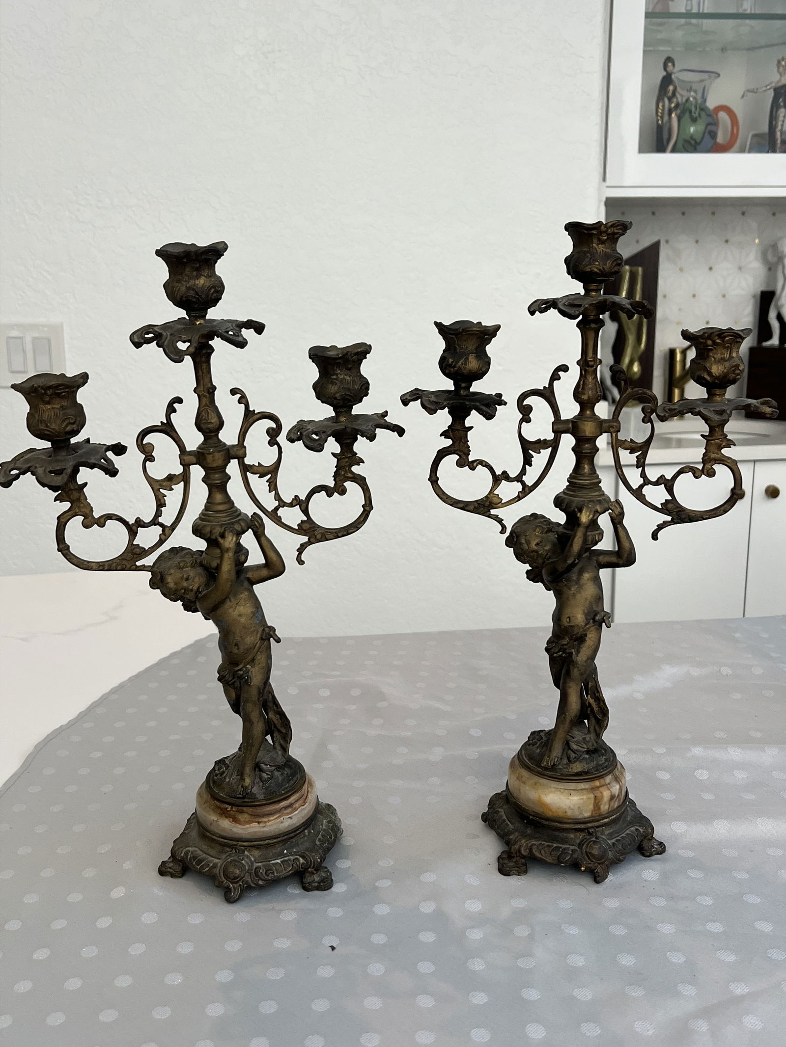 Pair of Antique Figural Candleabra: Victorian candleabra pair with marble bases, putti or winged cherub figures. Dimensions: H 16" x W 9" Condition: Some wear to patina finish and tarnish to bases. Low Estimate: 200.00High Estimate: