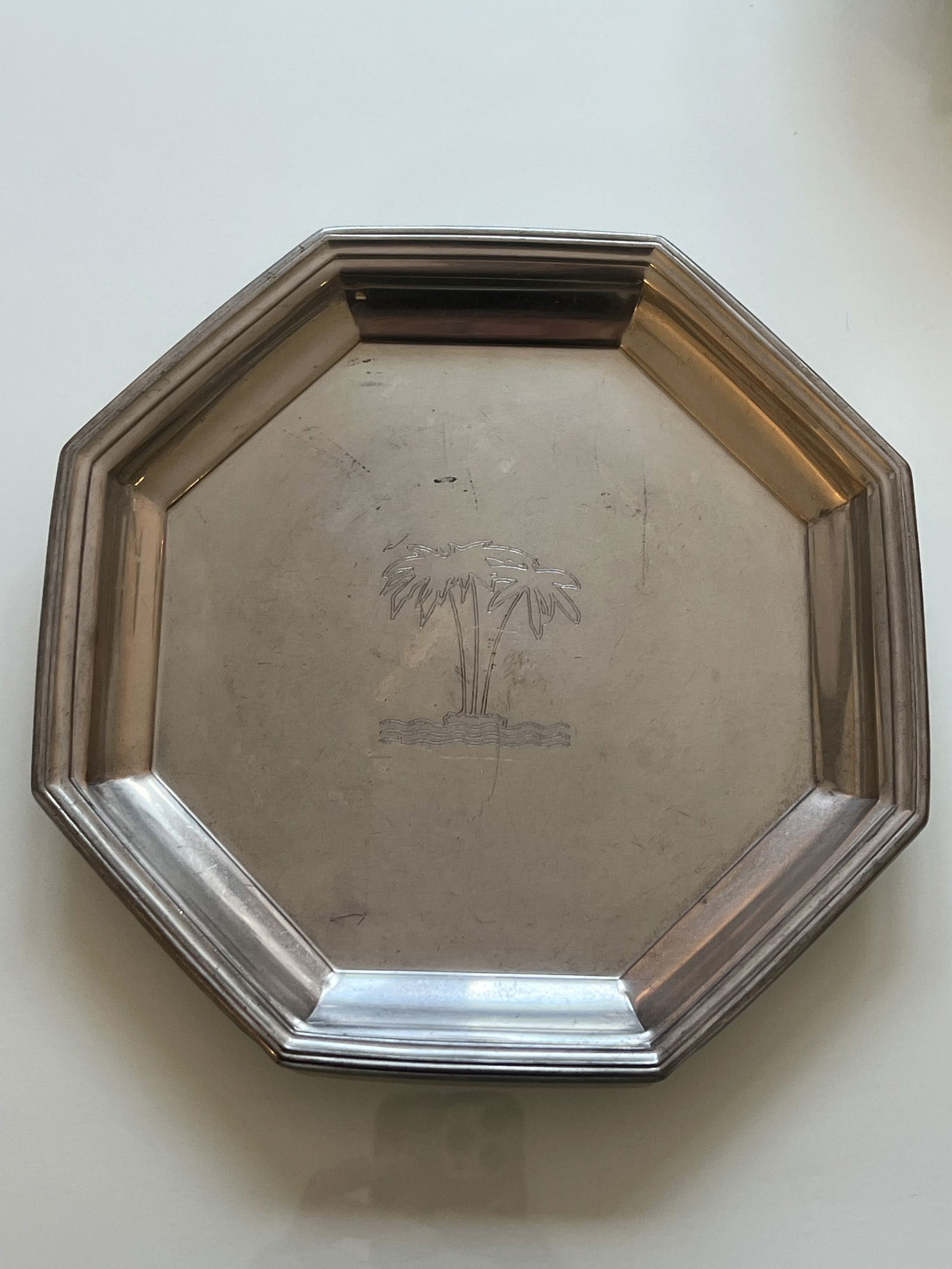 Octagonal Silver tone Palm Tree Tray: A silverplate? Art Deco style tray with an etched palm tree. Dimensions: 9" Condition: Some surface scratching. Low Estimate: 10.00 High Estimate: 10000.00