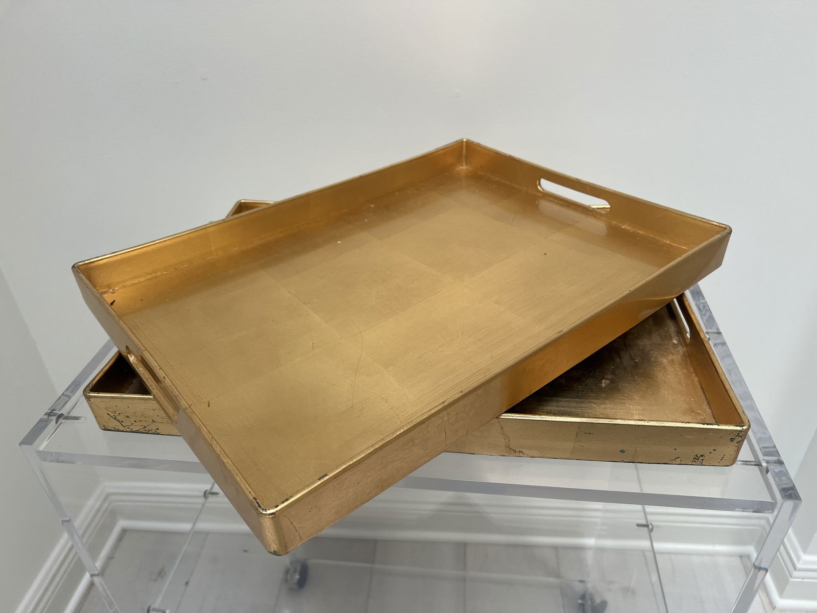 (2) Gold Gilt Style Dresser Trays: Serving, sofa or dresser trays. Faux gold gilt, Pier One. Dimensions: L 18.75" x W 14" Condition: Some marks and stains. Low Estimate: 10.00High Estimate: 10000.00