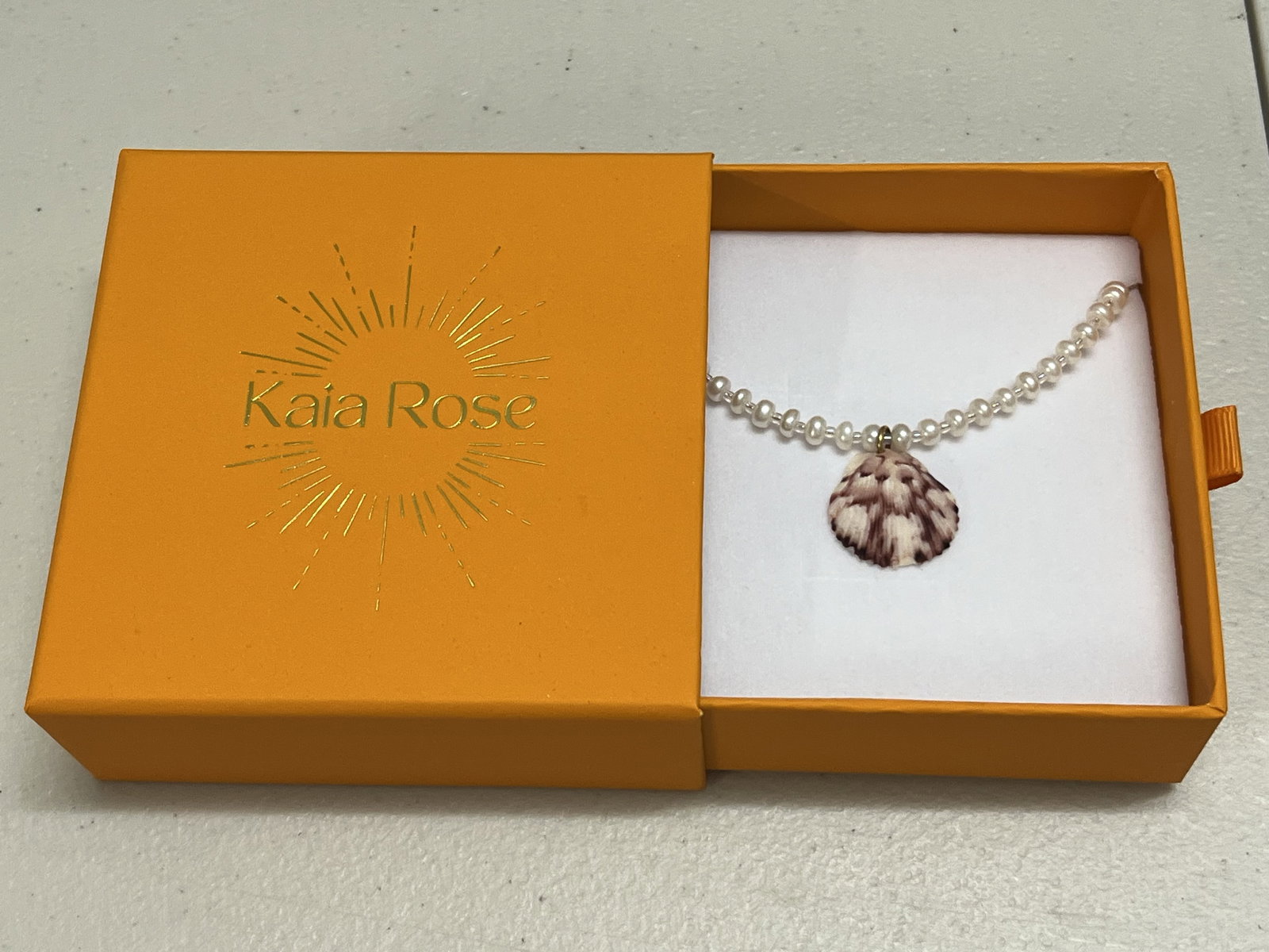 Kaia Rose Pearl and Shell Necklace: Pearl necklace with shell enhancer. Dimensions: L 18" Shell: 1" Condition: Like new in box. Low Estimate: 10.00 High Estimate: 10000.00