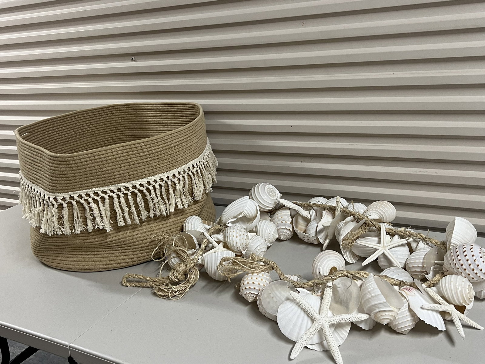 Coastal DÃ©cor Including Shells: A strung shell hanging and a boho woven beige basket. Dimensions: Large basket: H 13" x Dia: 24" Condition: Lightly used. Low Estimate: 10.00 High Estimate: 10000.00
