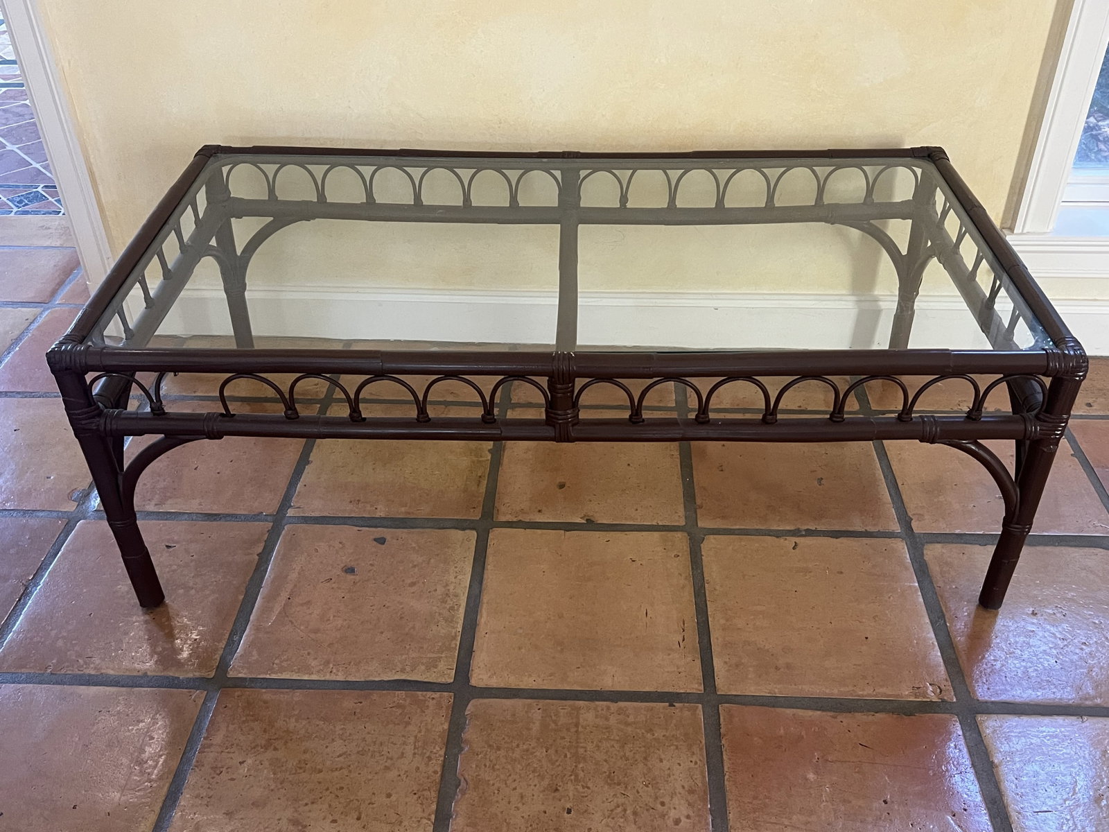 Bamboo Rattan Coffee Table: Glass top, brown color. Dimensions: L 46" x W 24" x H 16" Condition: One hoop is broken, see picture. Scallop chip to edge of glass. Low Estimate: 10.00 High Estimate: 10000.00
