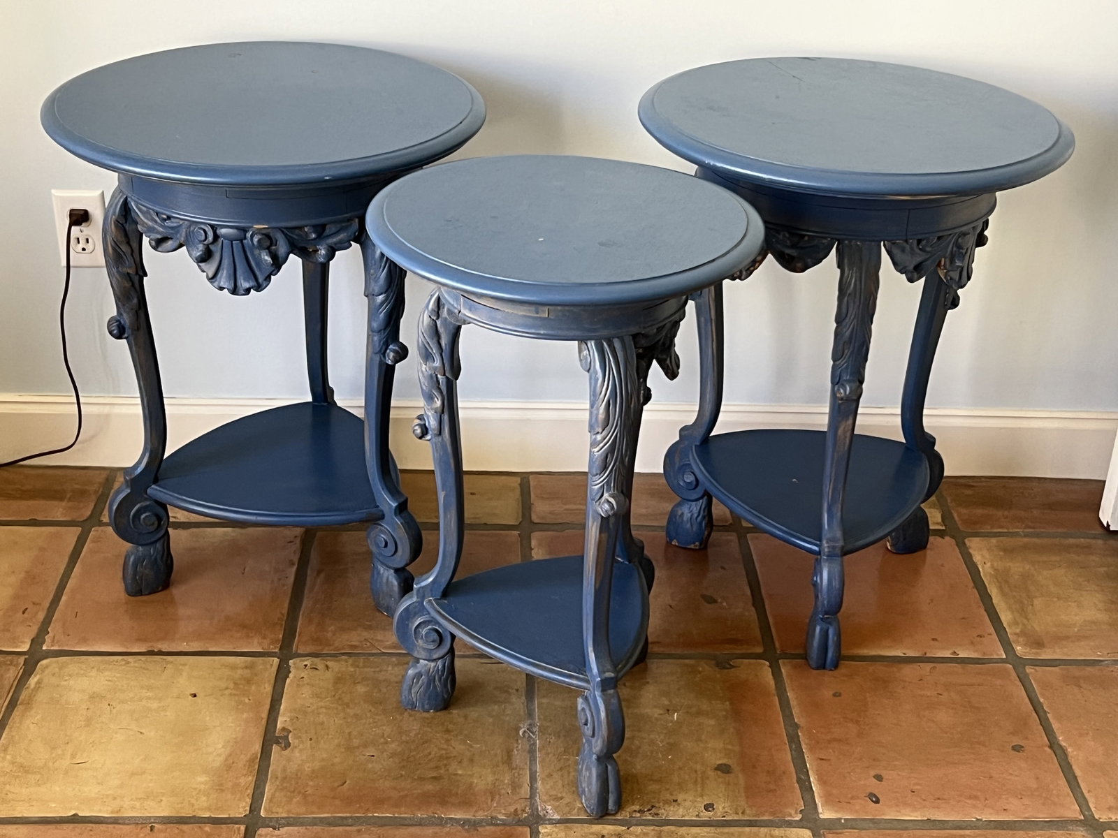 (3) Antique Blue Painted Side Tables: A trio of nicely made, solid wood antique tables with split hooved feet, flanking acanthus leaves, shell accent and triangular shelf. Dimensions: larger: H 25.5" x Dia: 20" Smaller: H 25" x Dia: 16"